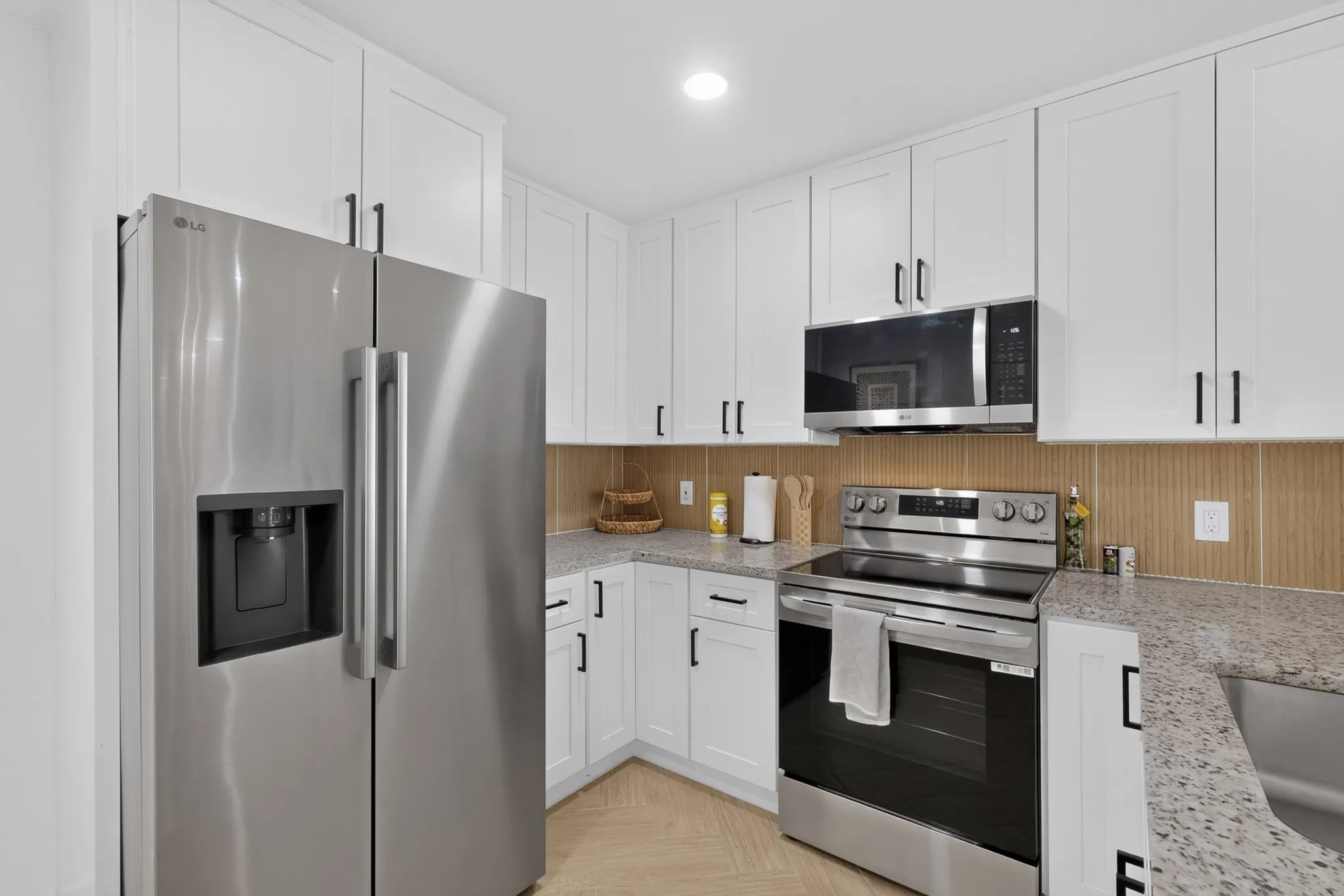 Stainless steel appliances, white shaker-style cabinetry, light speckled countertops, and a full-height tiled backsplash