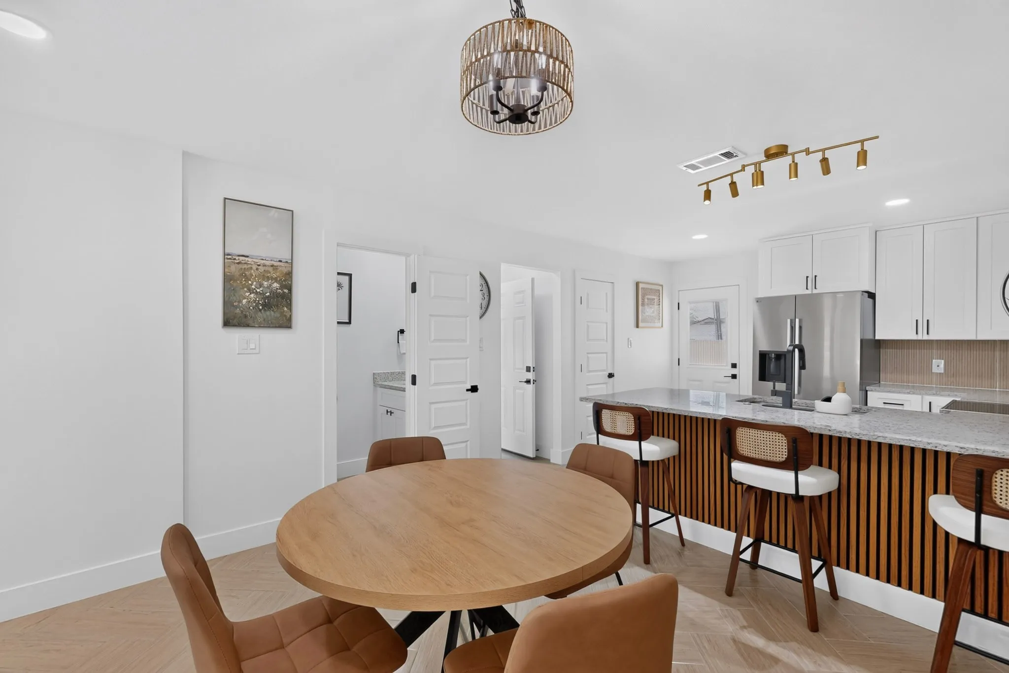 Open-concept kitchen and dining area featuring a wood-finish floor, white cabinetry, integrated stainless steel refrigerator, and a kitchen island with a textured wood base