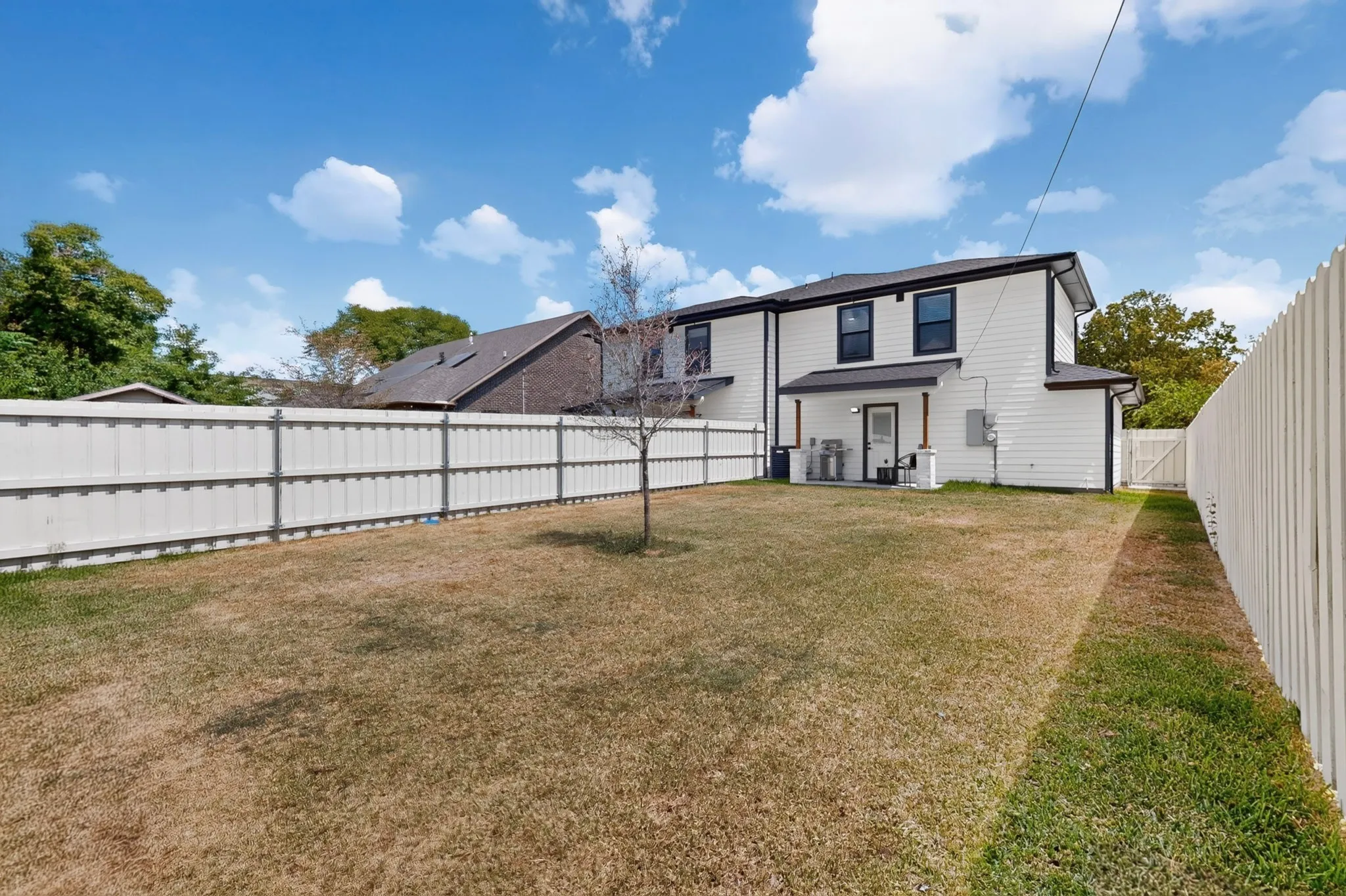 Expansive lawn bordered by a white privacy fence and rear white siding exterior with a covered patio
