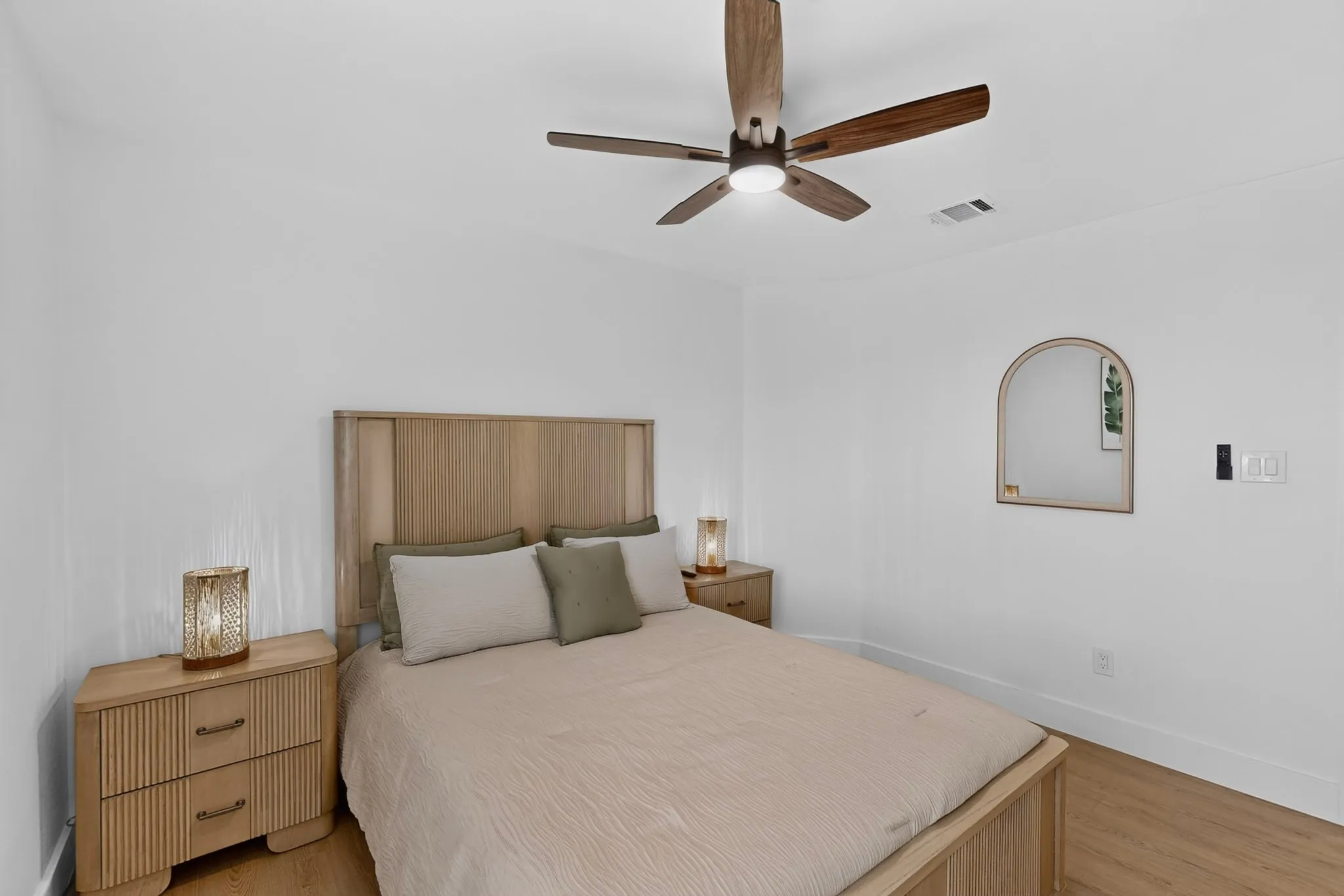 White walls, wood-finish flooring, and a ceiling fan with integrated lighting