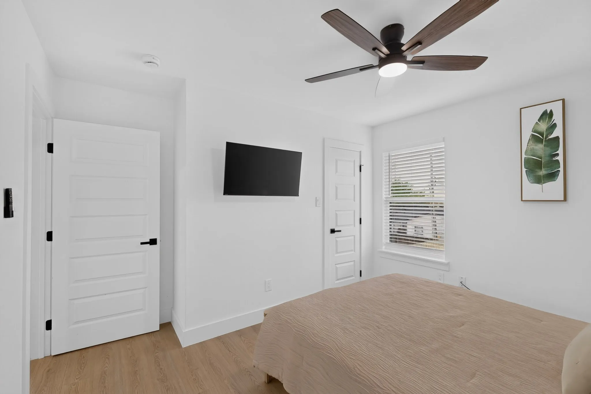 Wood-finish flooring, white paneled door, modern ceiling fan with lighting, window with blinds, and white walls