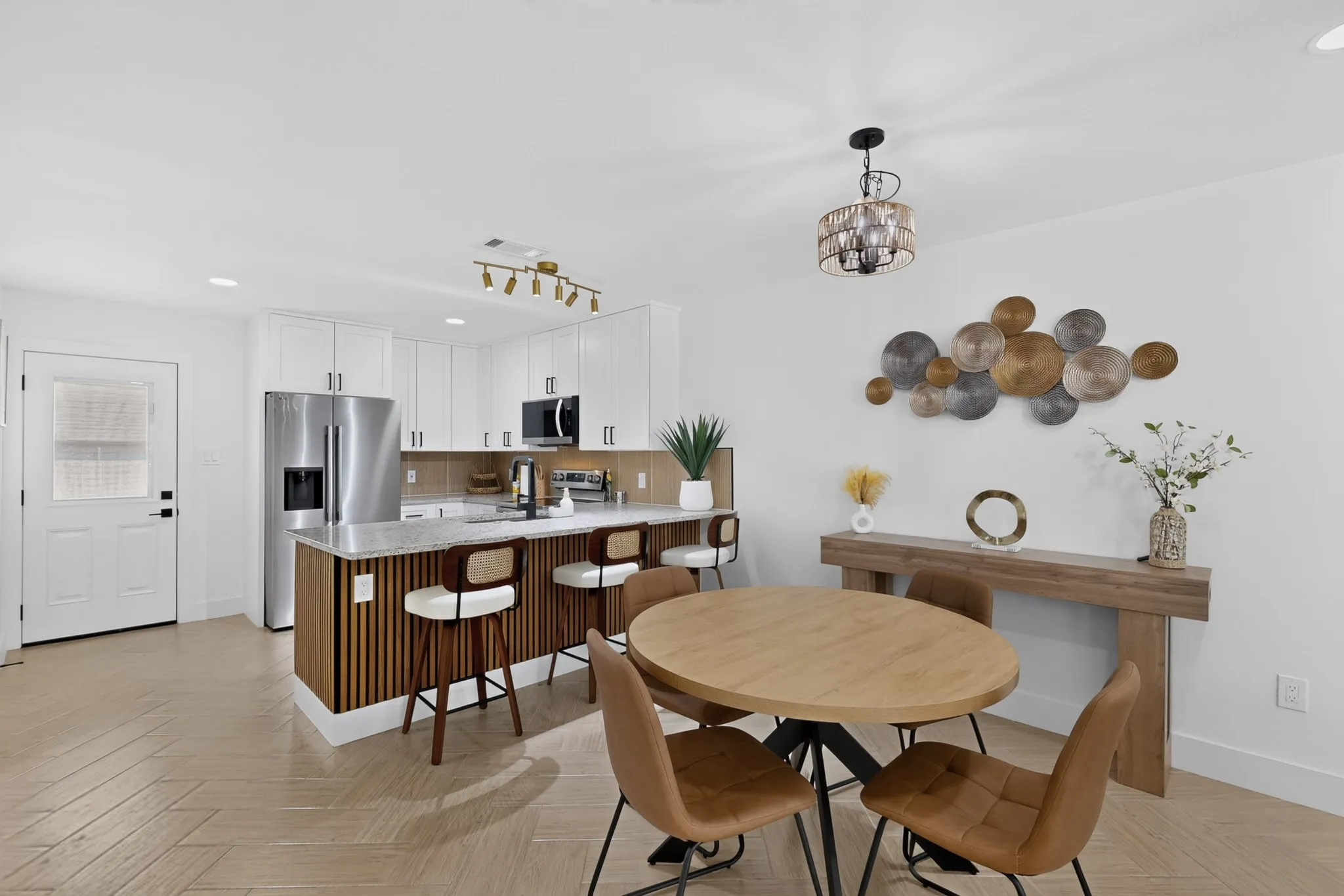 Open-concept living space with wood-finish flooring, a kitchen island with built-in seating, white cabinetry, and stainless steel appliances