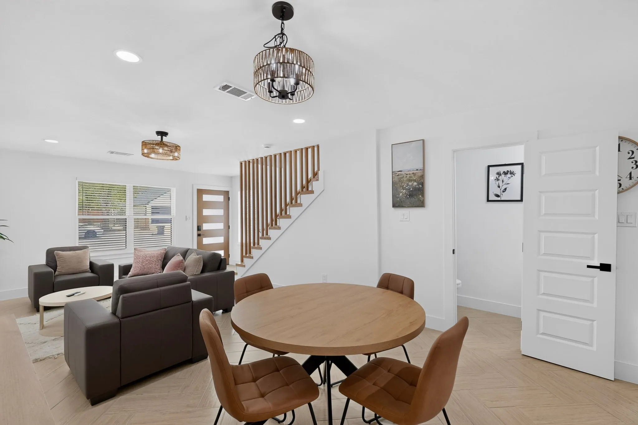 Open-concept living and dining area featuring wood-finish flooring, recessed lighting, and a modern wood slat staircase