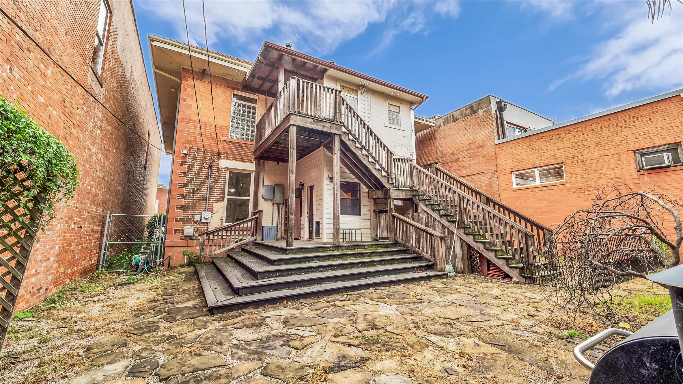 Rear exterior featuring a multi-level wood deck with stairs, stone patio, and brick facade