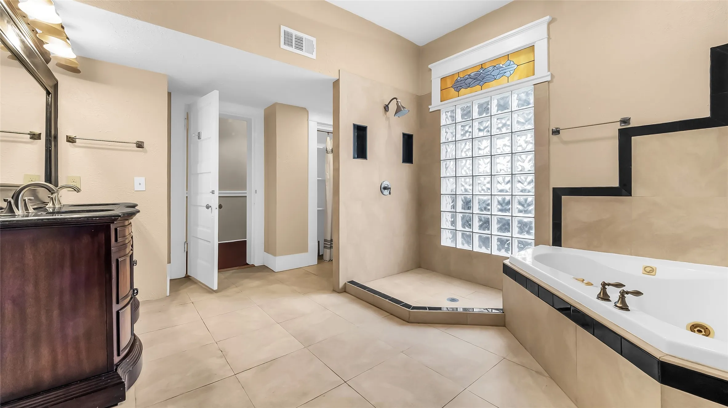 Tile flooring, built-in bathtub, glass block shower enclosure, stained glass window accent, and a built-in vanity with a dark countertop