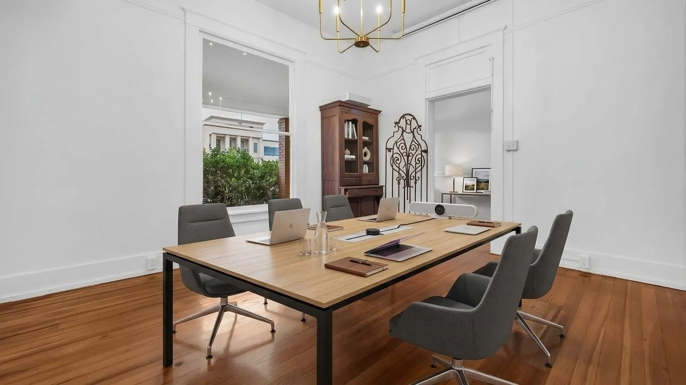 Sophisticated conference room showcasing warm wood-finish flooring, a substantial wooden table with black metal framing, and modern upholstered chairs