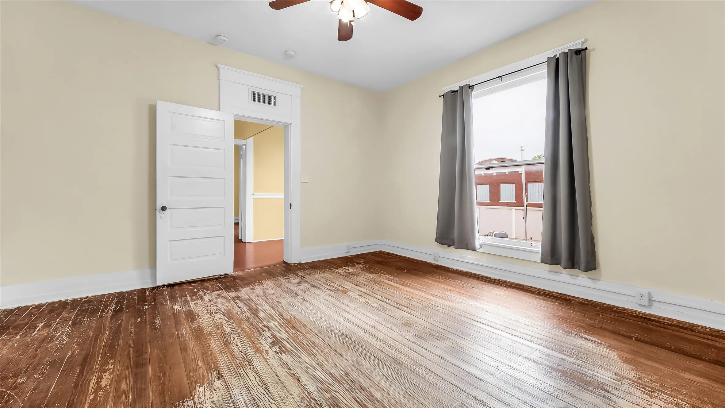Wood-finish flooring, paneled interior door, window with white trim, ceiling fan light fixture, and crown molding