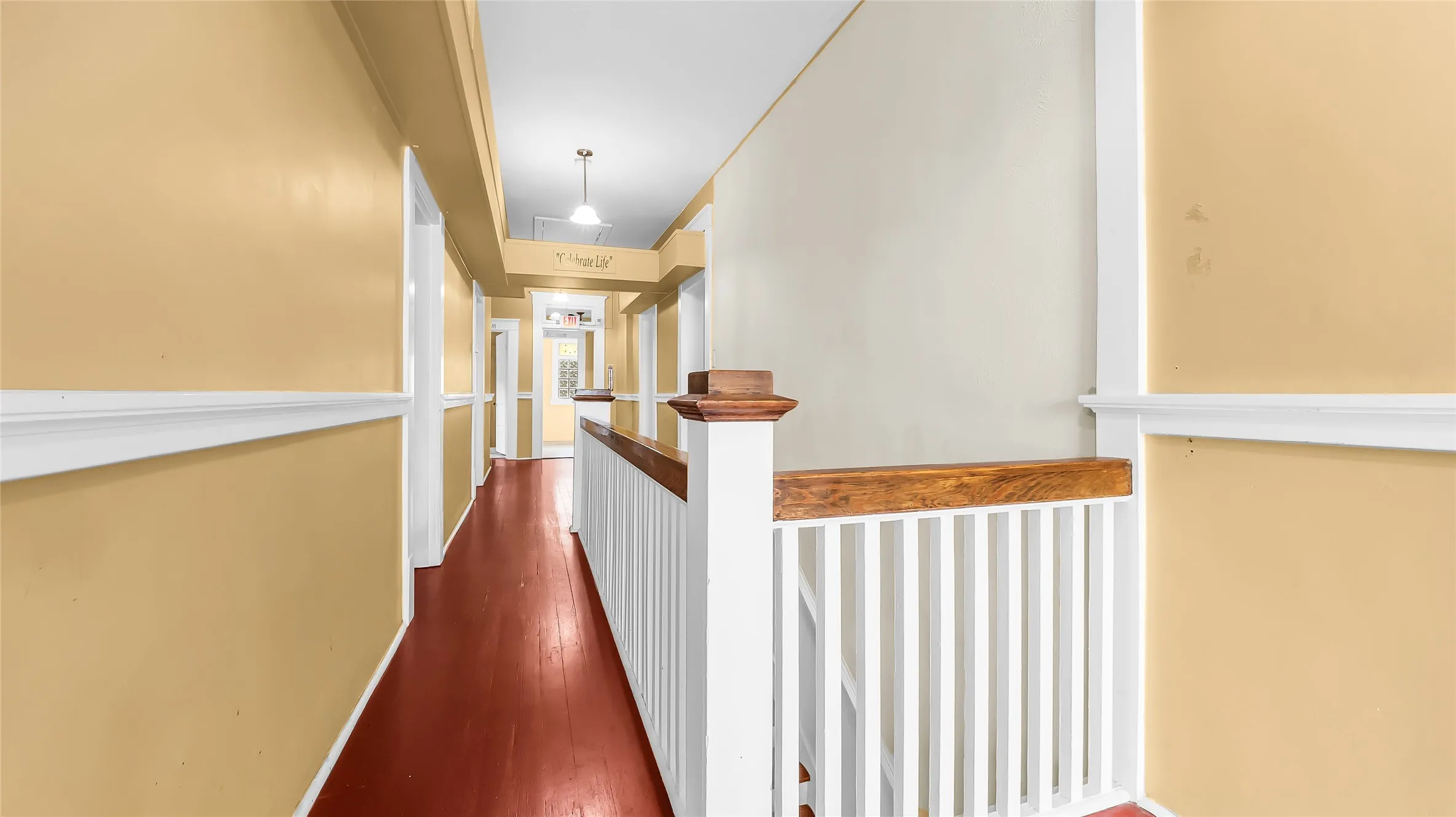 Hardwood flooring extending through the hallway, white painted handrail with wood-finish top, white chair rail molding, and a pendant light fixture