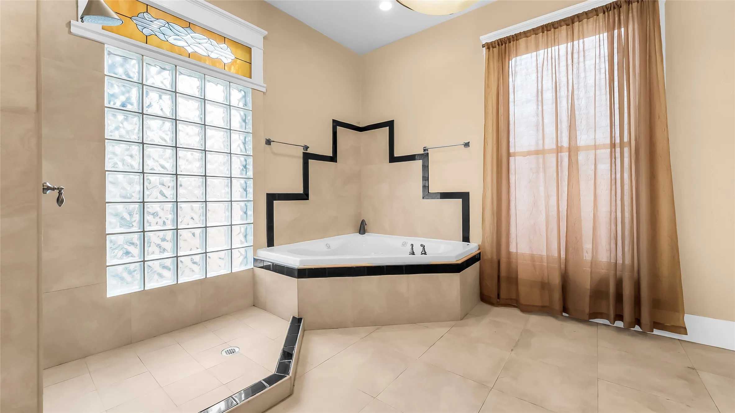 Spacious bathroom featuring an integrated shower area, glass block window, stained glass transom, corner soaking tub, and floor-to-ceiling window