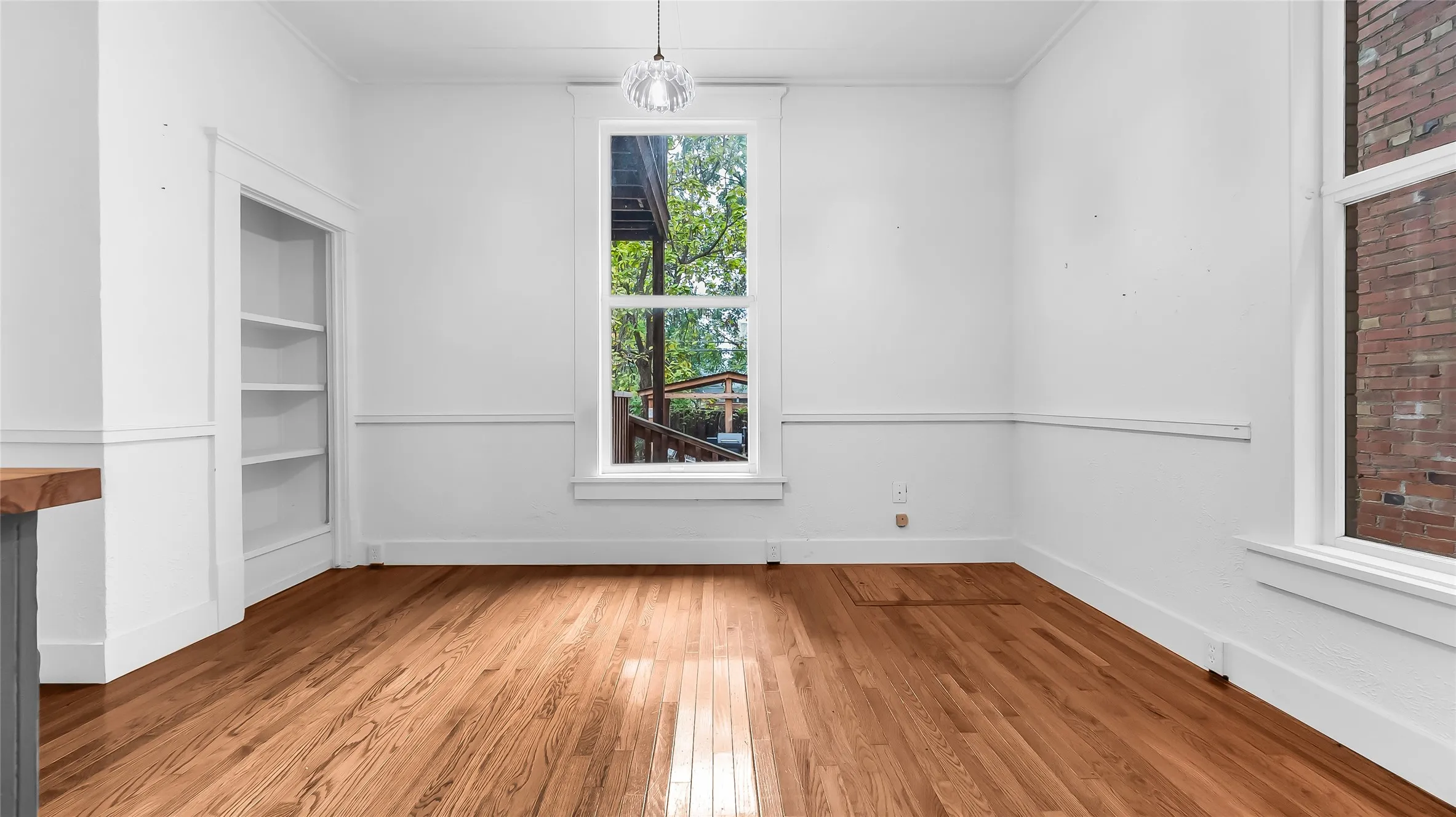 Hardwood flooring, built-in shelving, large windows, crown molding, and white wall paneling