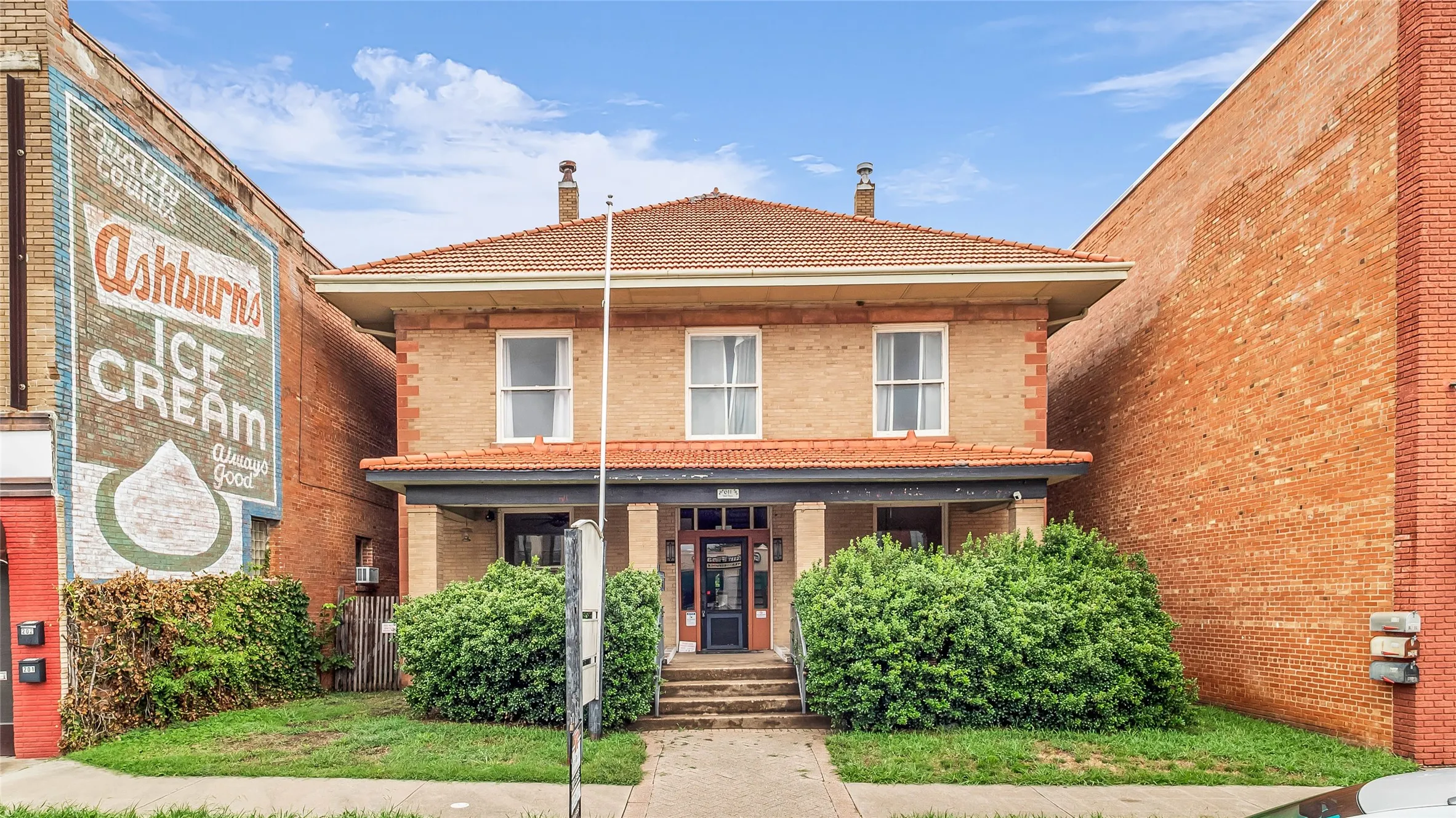 Two-story brick exterior with a tiled hip roof, featuring a covered porch entry and mature front landscaping