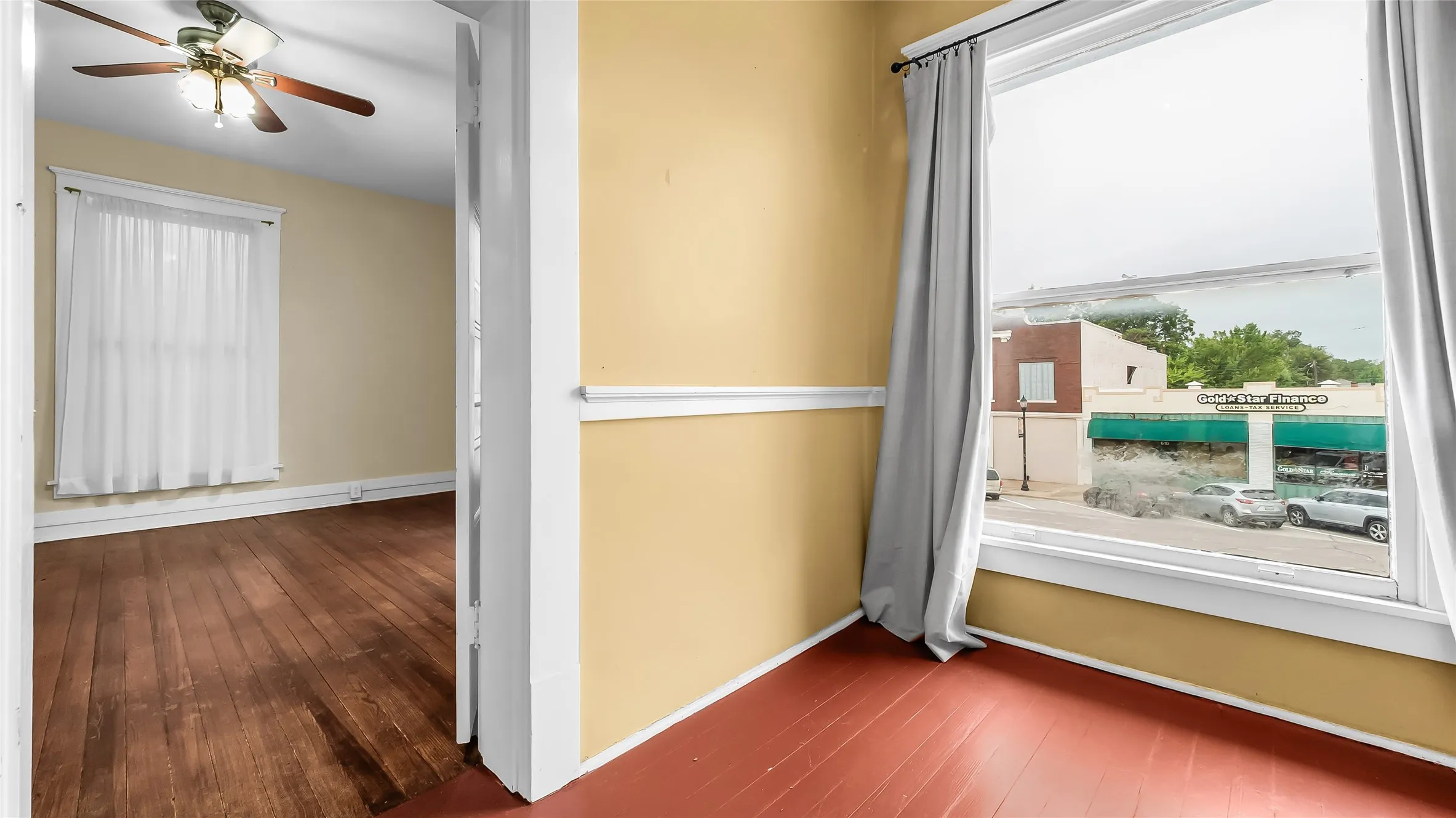 Wood-finish flooring, ceiling fan with integrated lighting, and multiple windows with trim