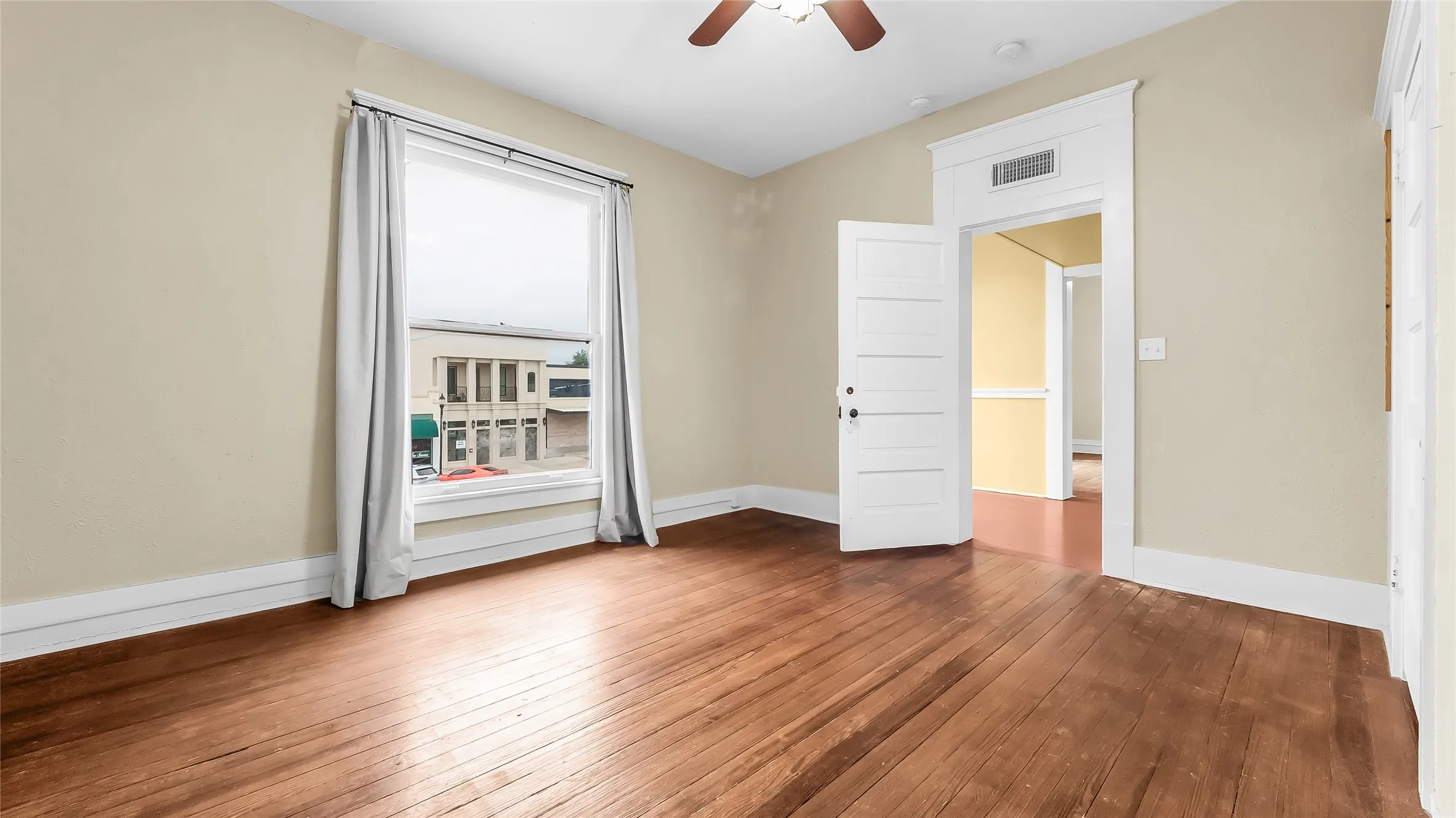 Hardwood flooring, ceiling fan, white trim, and a large window