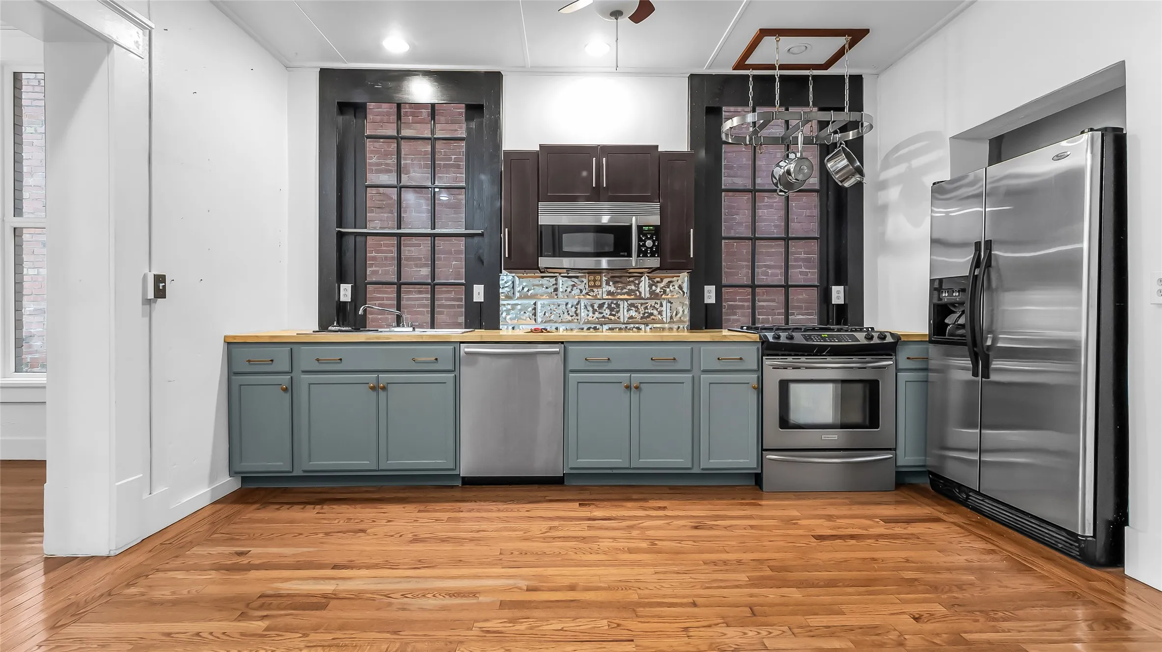 Hardwood flooring, stainless steel appliances, wood-finish countertops, custom tile backsplash, and dark-stained cabinetry