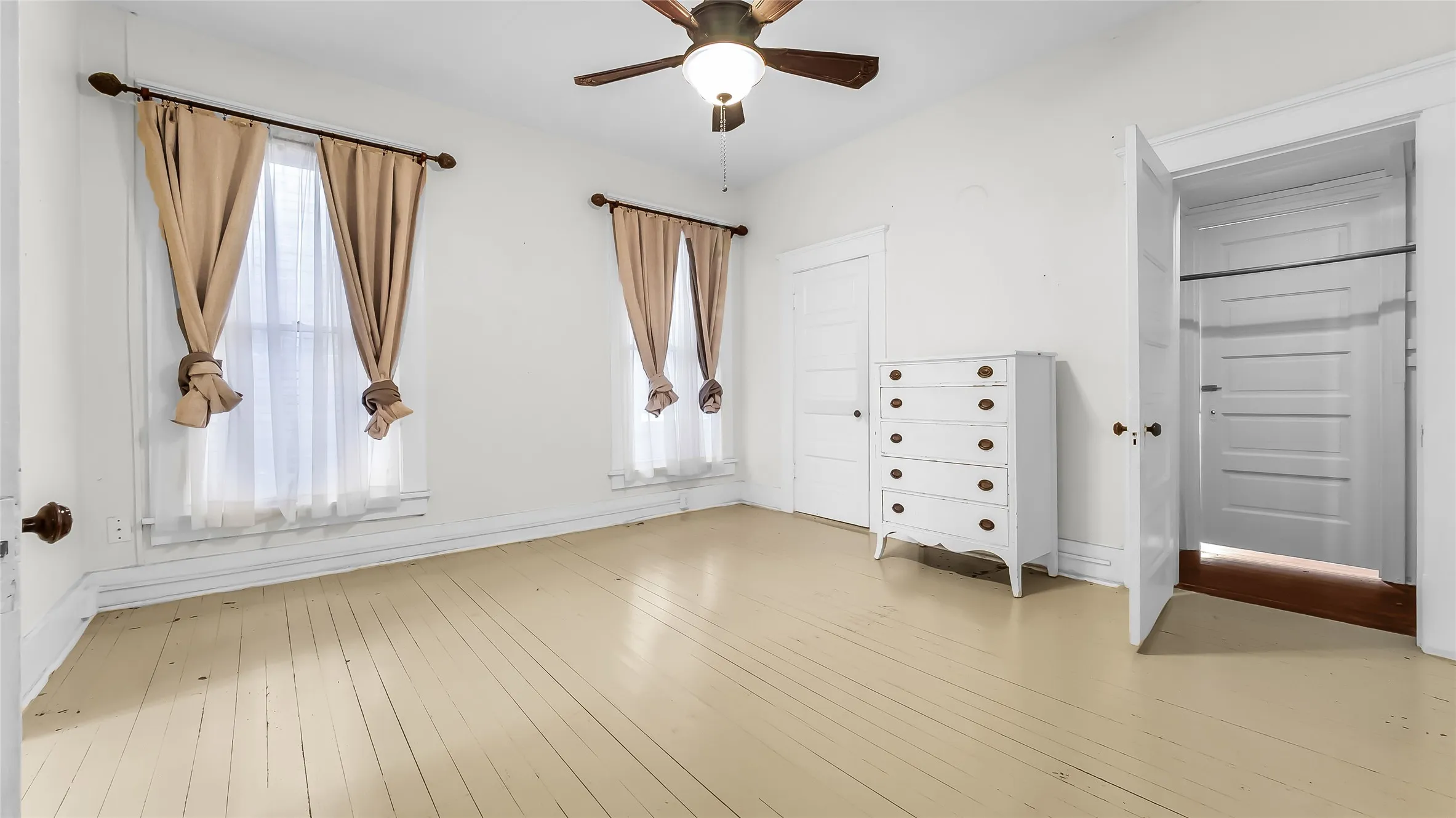 Bright room featuring light-toned wood flooring and a ceiling fan