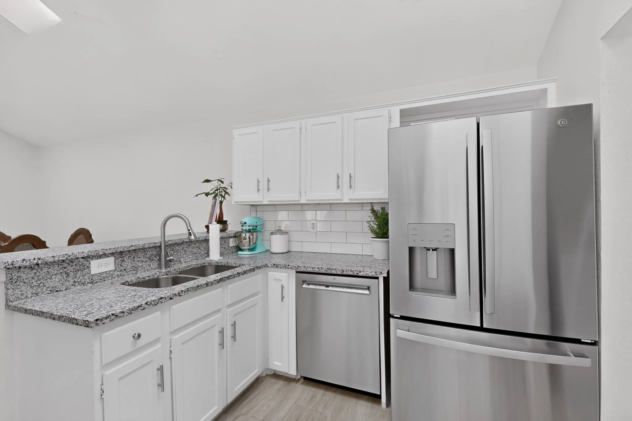 White shaker-style cabinetry, stainless steel appliances, dual basin undermount sink, subway tile backsplash, and light-toned wood-finish flooring