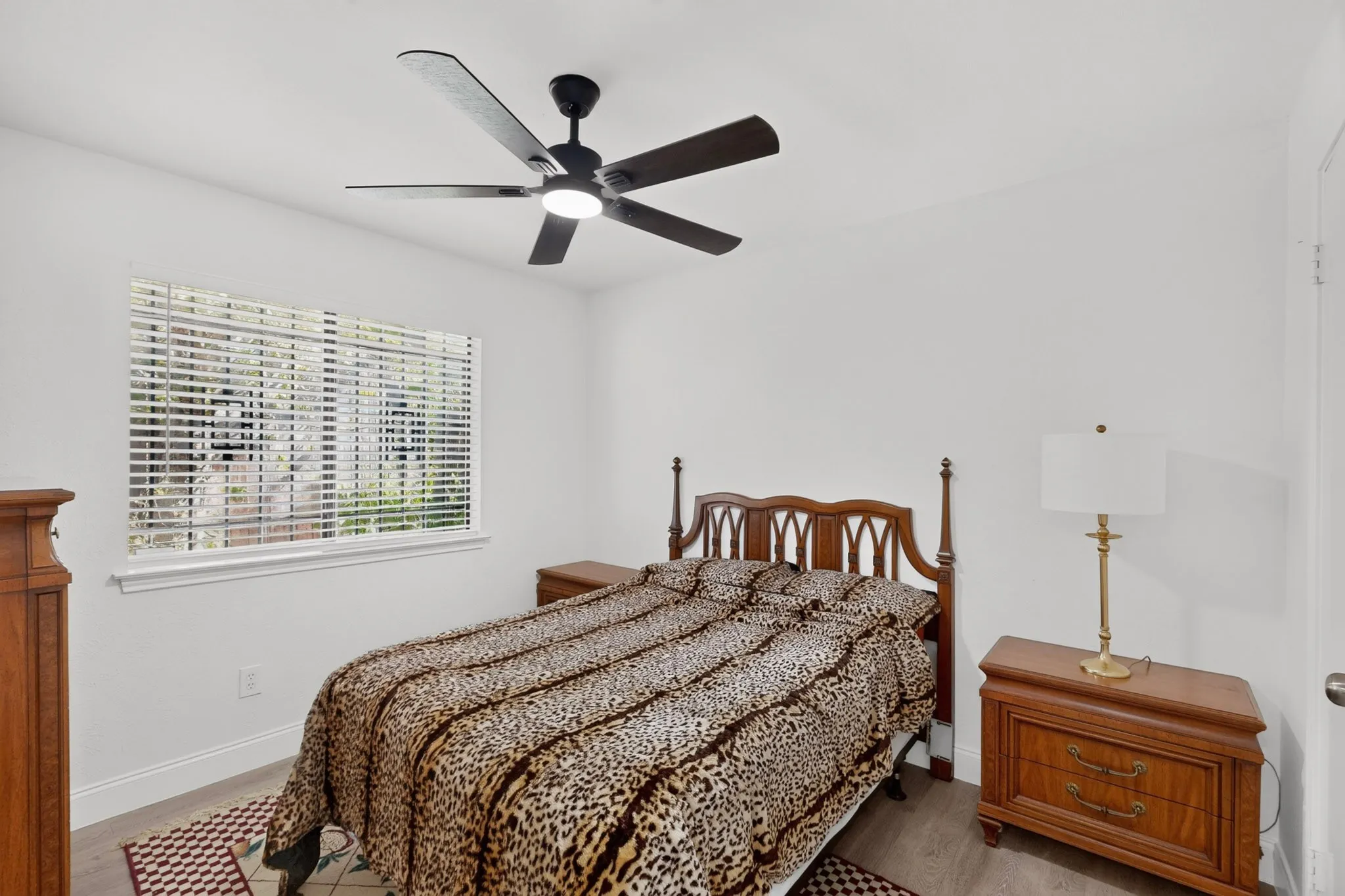 White walls, window with blinds, wood-finish flooring, and a ceiling fan with integrated lighting