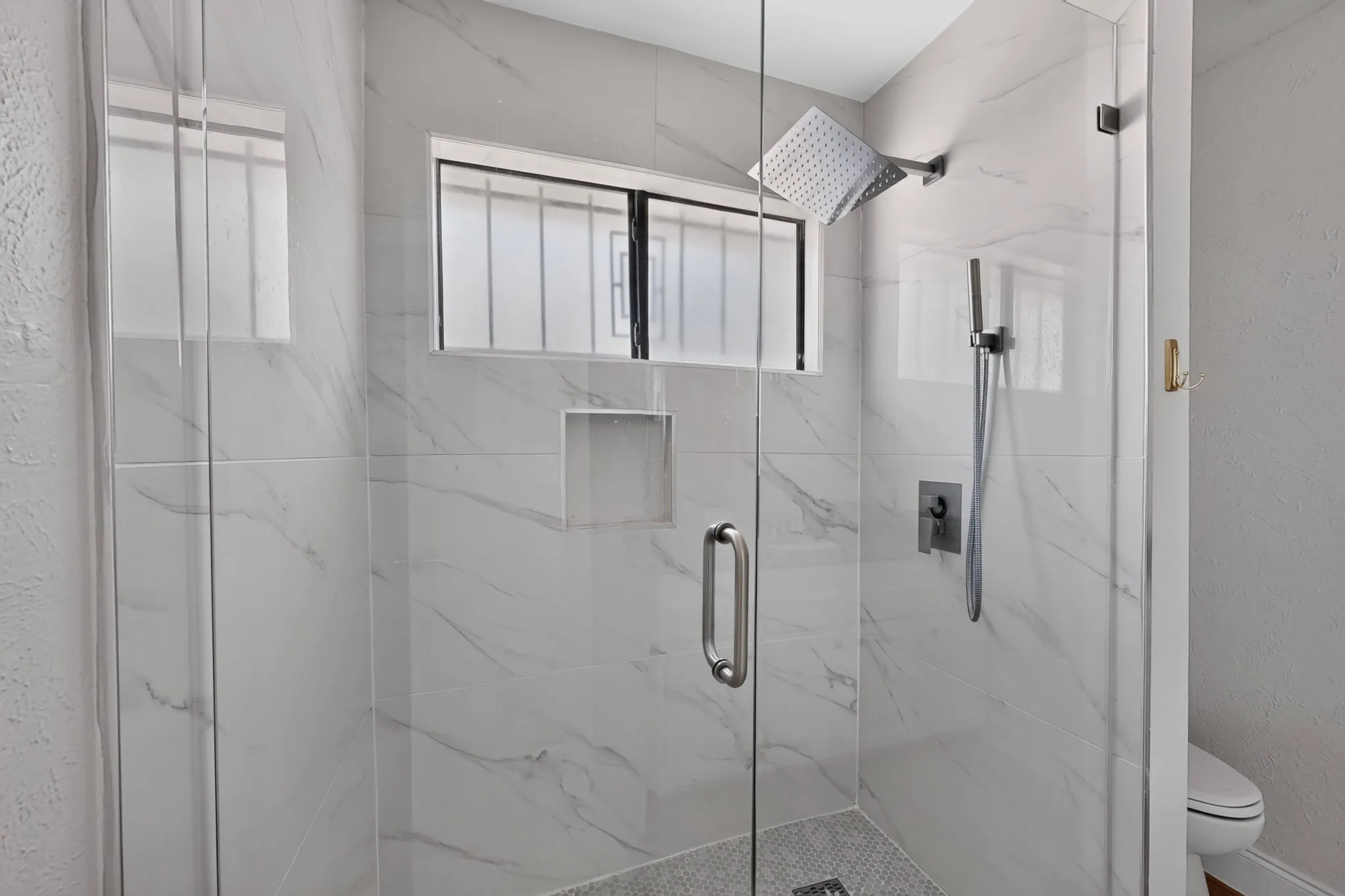 Glass-enclosed shower featuring white marble-look tile, a built-in shower niche, and a rain showerhead