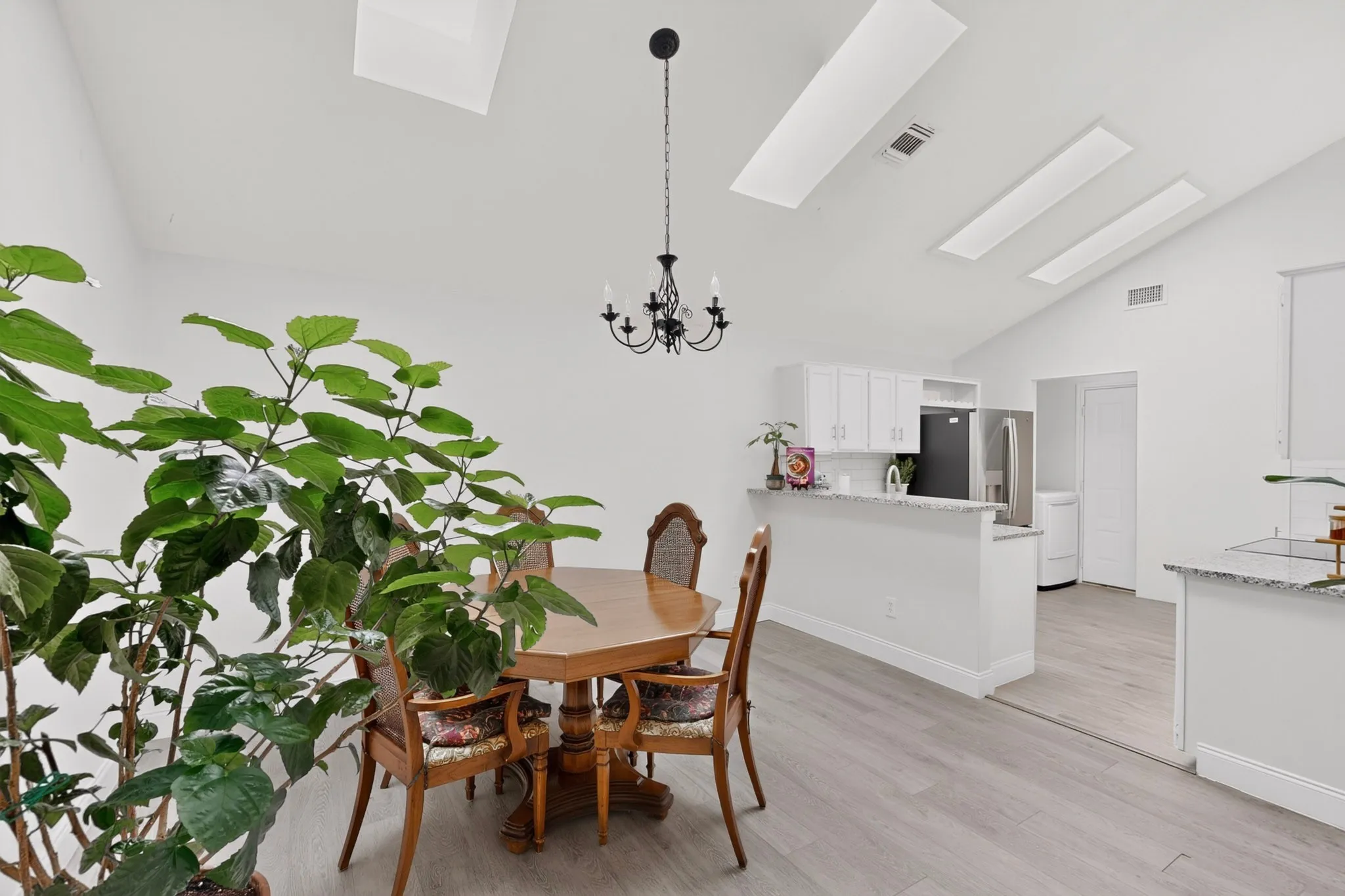Vaulted ceiling with skylights, wood-finish flooring, white cabinetry, granite-finish countertops, and black and stainless steel appliances
