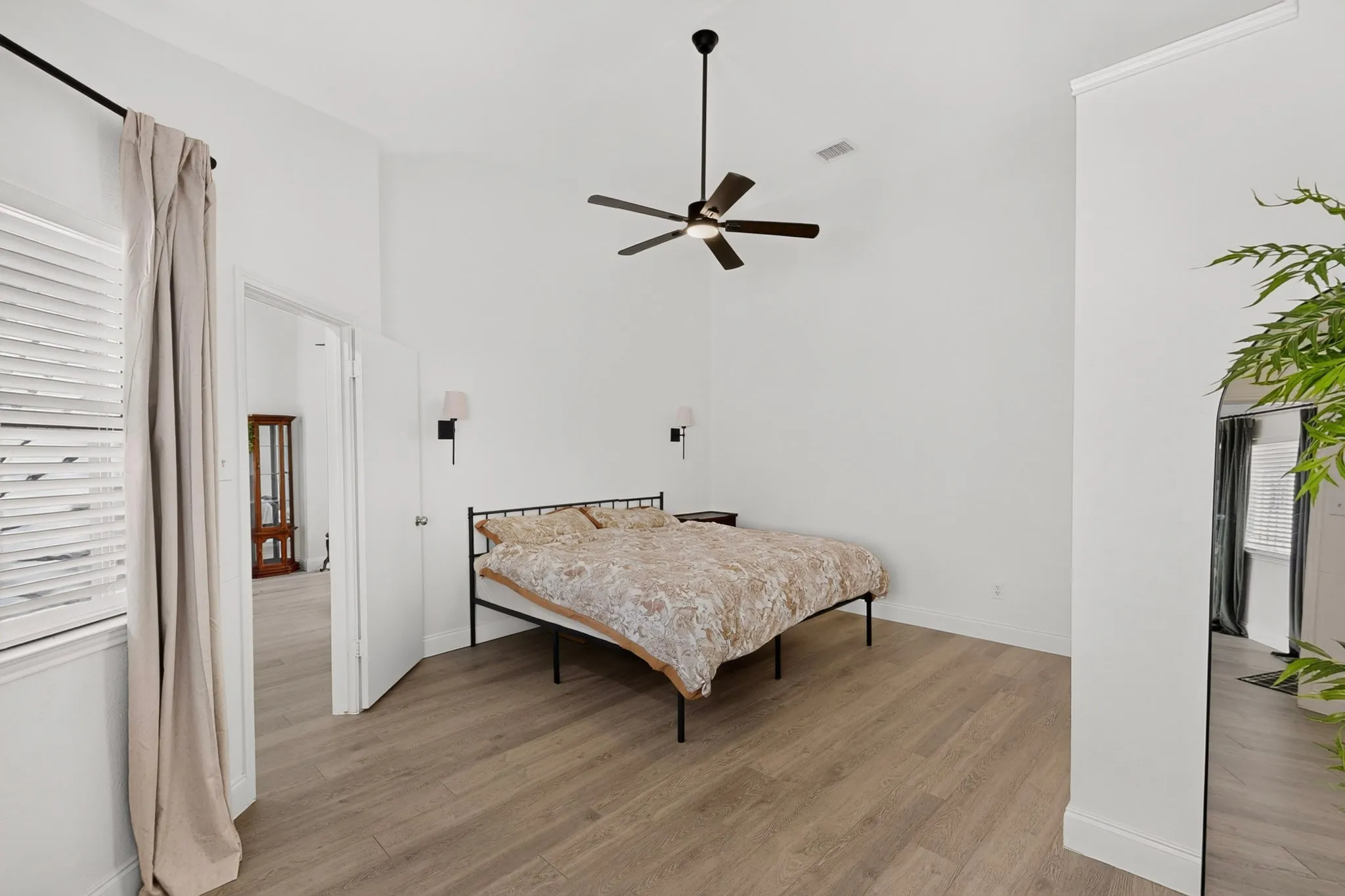 Vaulted ceiling with a ceiling fan, wood-finish flooring, plantation-style window shutters, and wall-mounted sconces