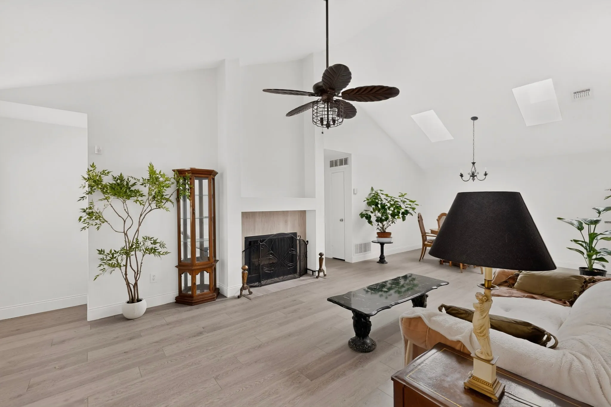 Vaulted ceiling with skylights, wood-finish flooring, fireplace with a hearth, and a ceiling fan with integrated lighting