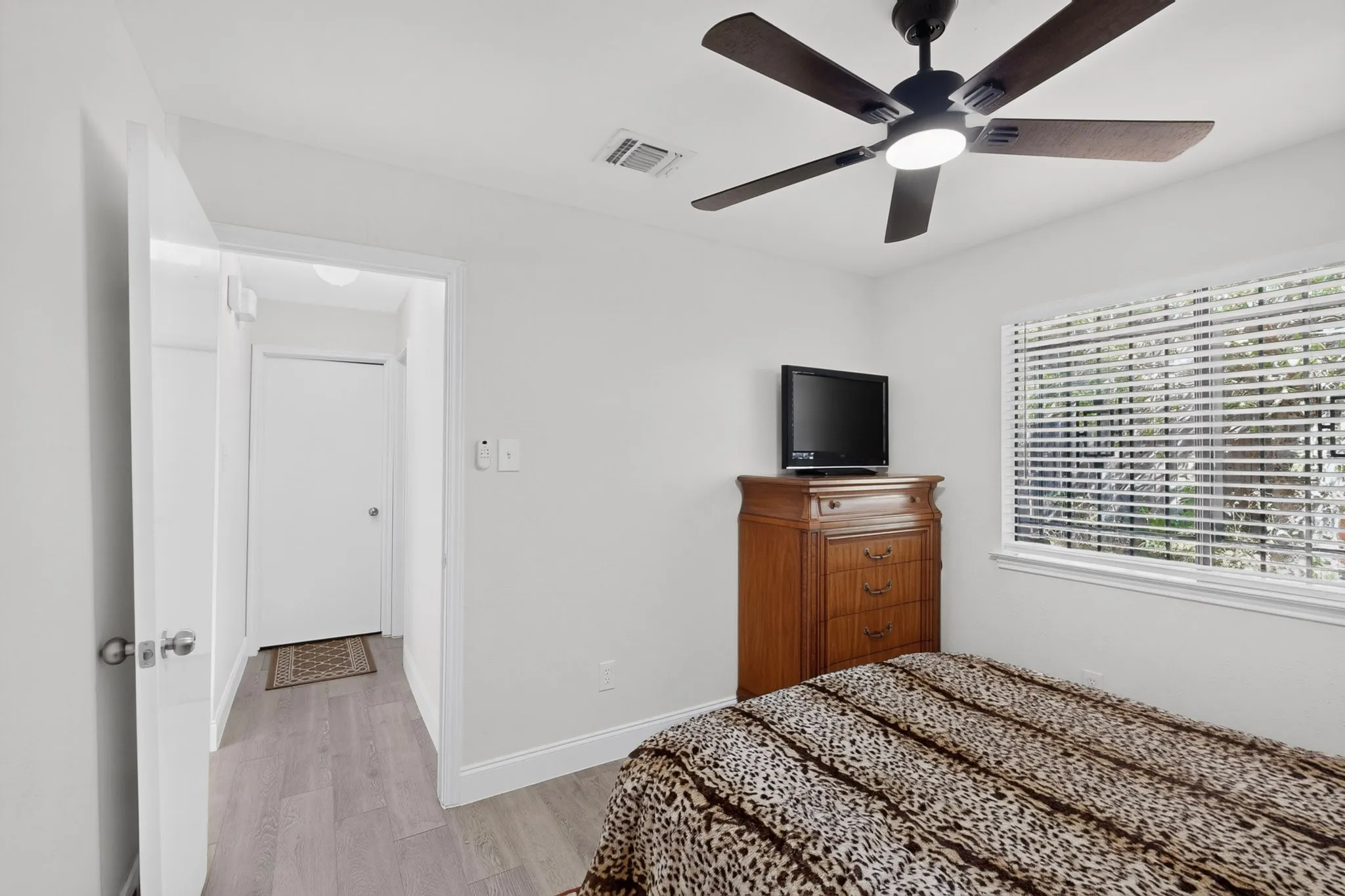 Wood-finish flooring, white walls, and a ceiling fan with integrated lighting