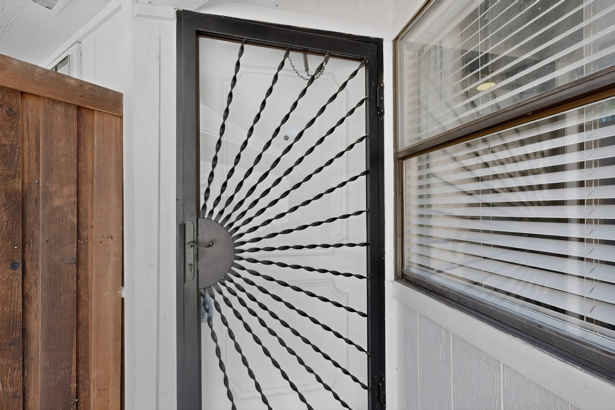 Decorative security screen door with a sunburst design, adjacent to a window with horizontal blinds
