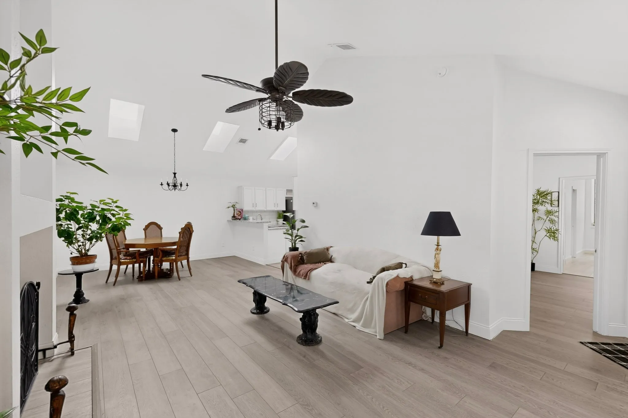 Vaulted ceilings with skylights, wood-finish flooring, white walls, and a ceiling fan with integrated lighting