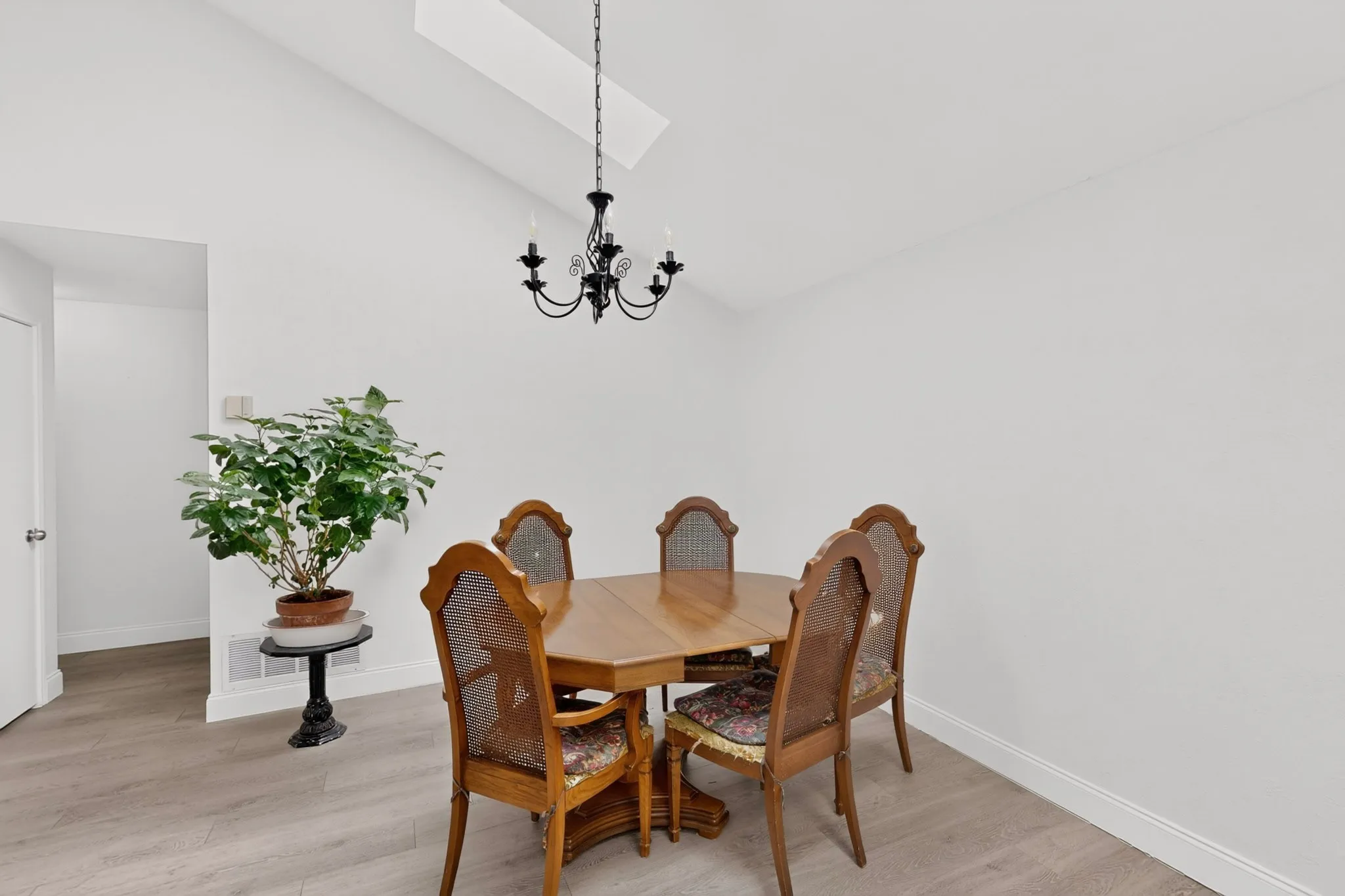 Vaulted ceiling with skylight, black chandelier, and wood-finish flooring