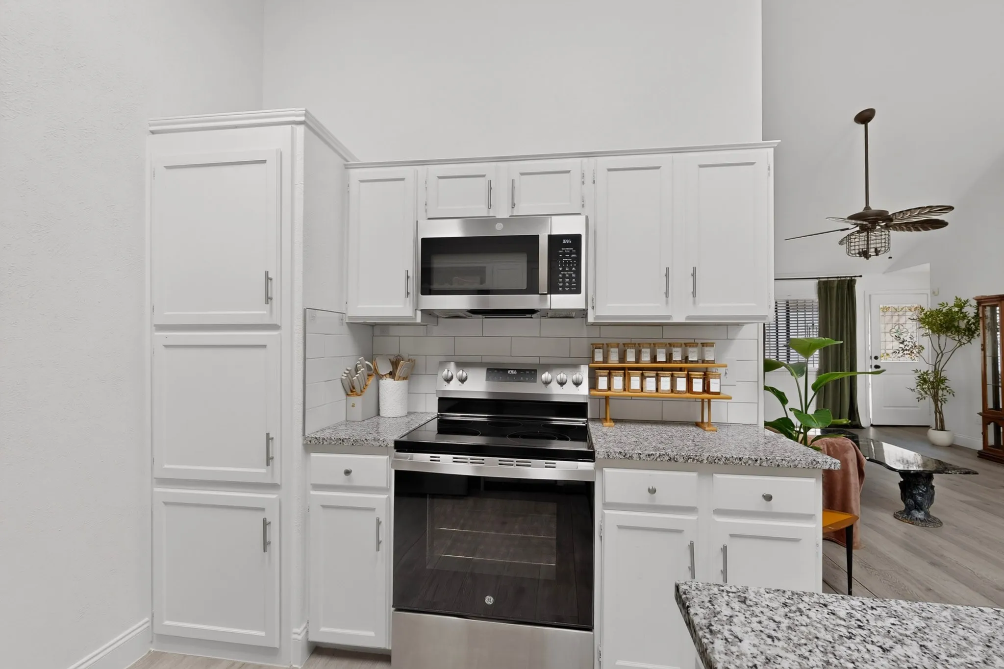 White cabinetry with brushed nickel hardware, stainless steel appliances, speckled countertops, and subway tile backsplash