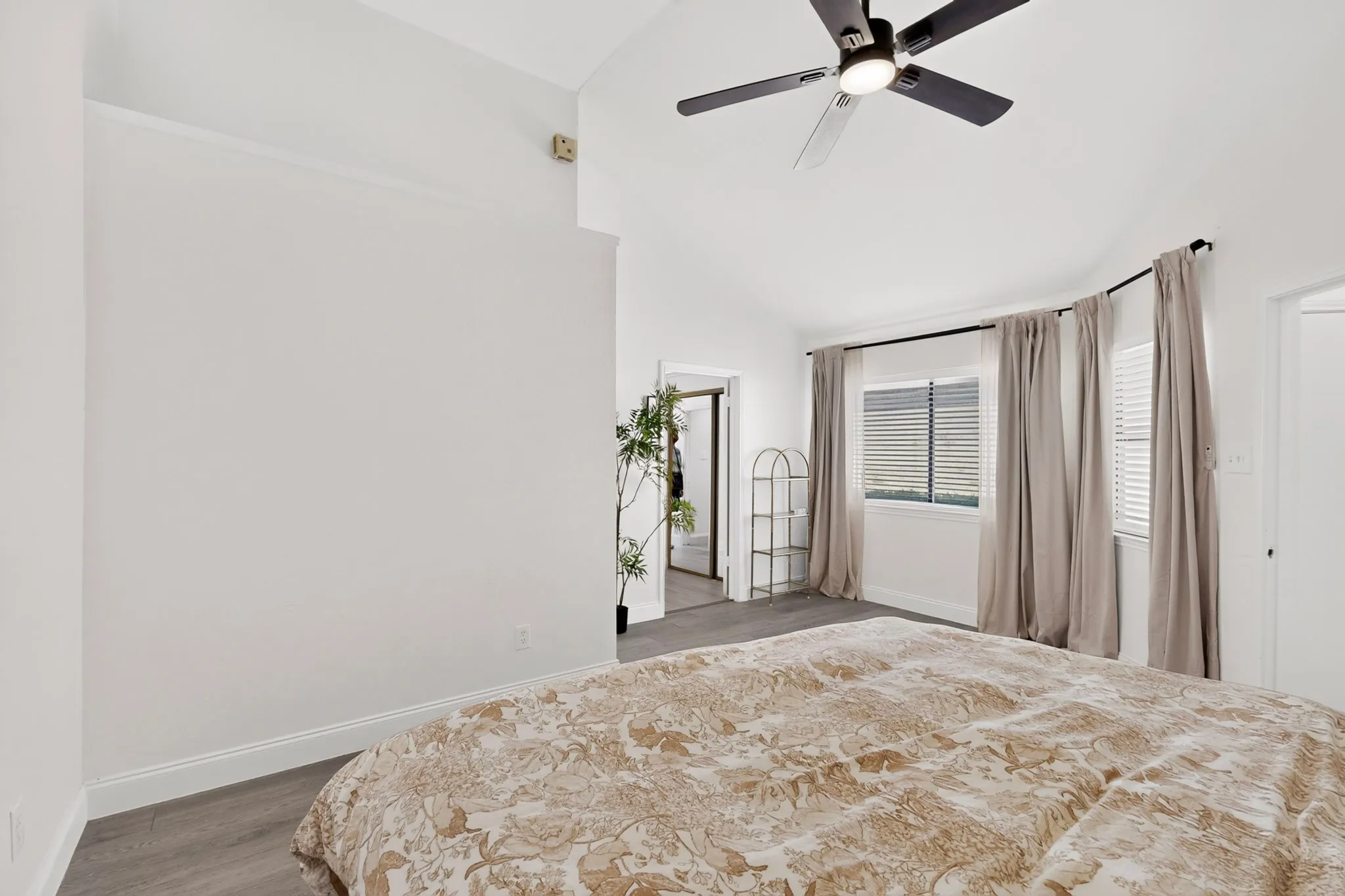 Vaulted ceiling featuring a ceiling fan, wood-finish flooring, and multiple windows with blinds