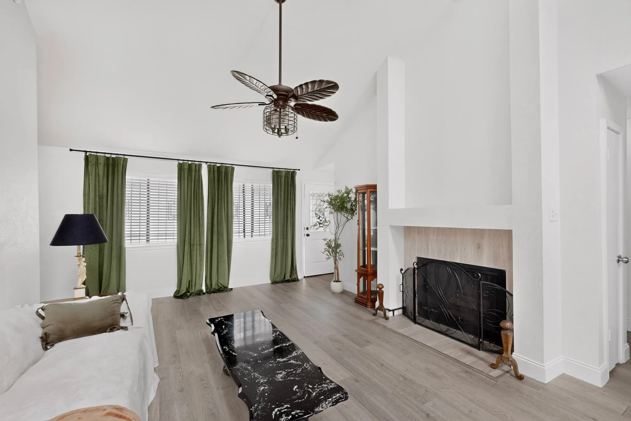 Vaulted ceilings with a ceiling fan, fireplace with a hearth, multiple windows with blinds, and wood-finish flooring