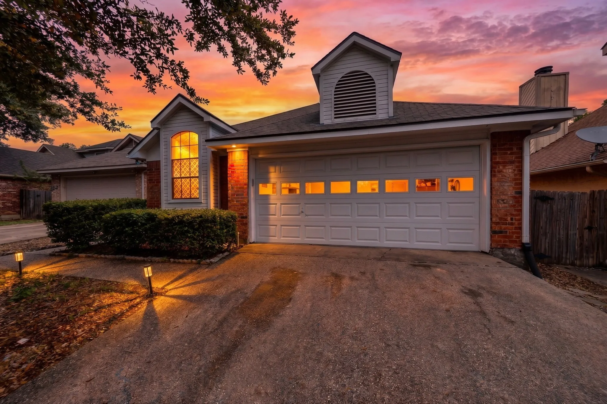 Brick and siding exterior with a prominent arched window, attached garage with panel detailing, and a dormer featuring a louvered vent