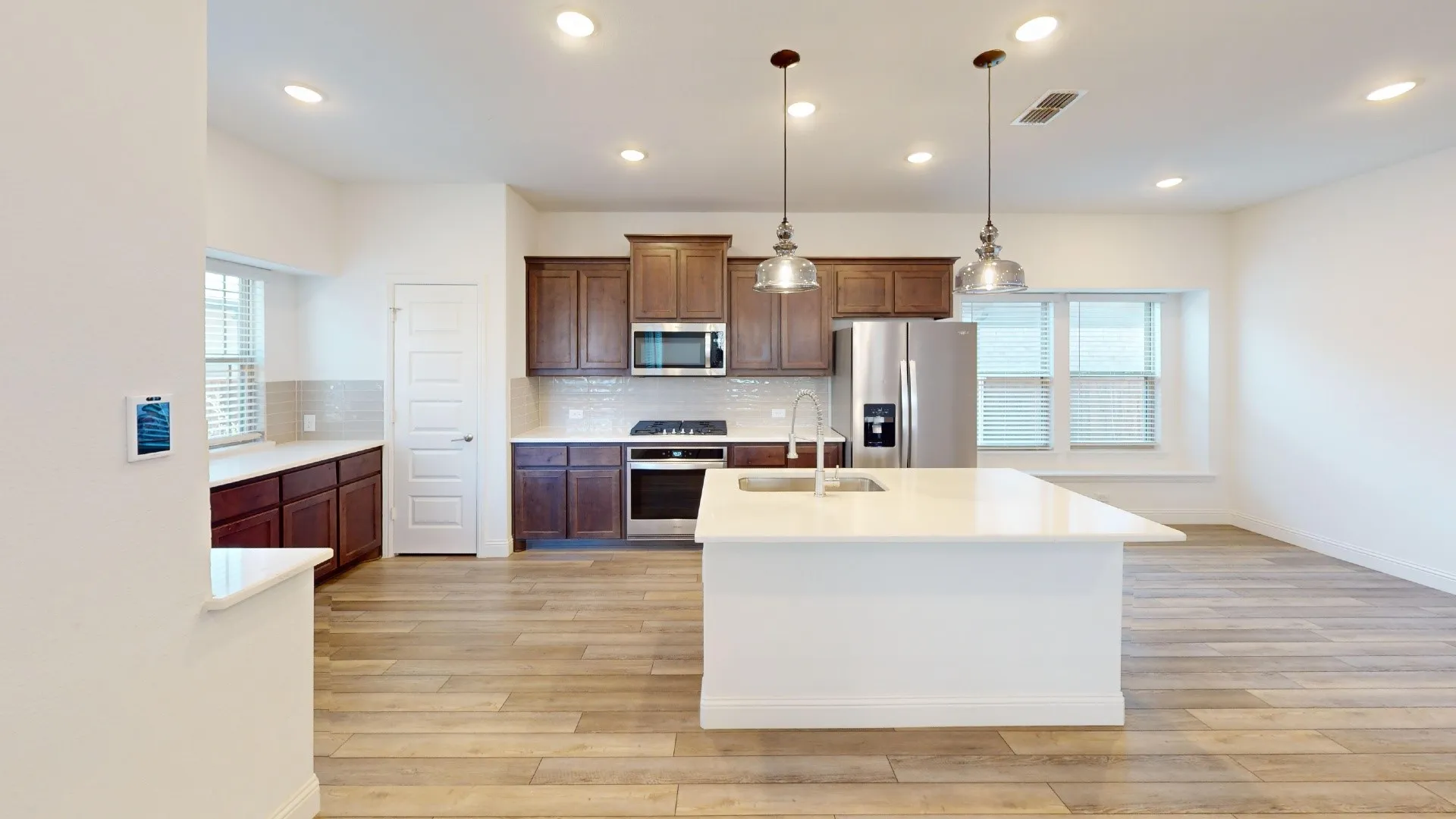 Open-concept kitchen featuring an expansive island, wood-finish flooring, recessed lighting, and stainless steel appliances