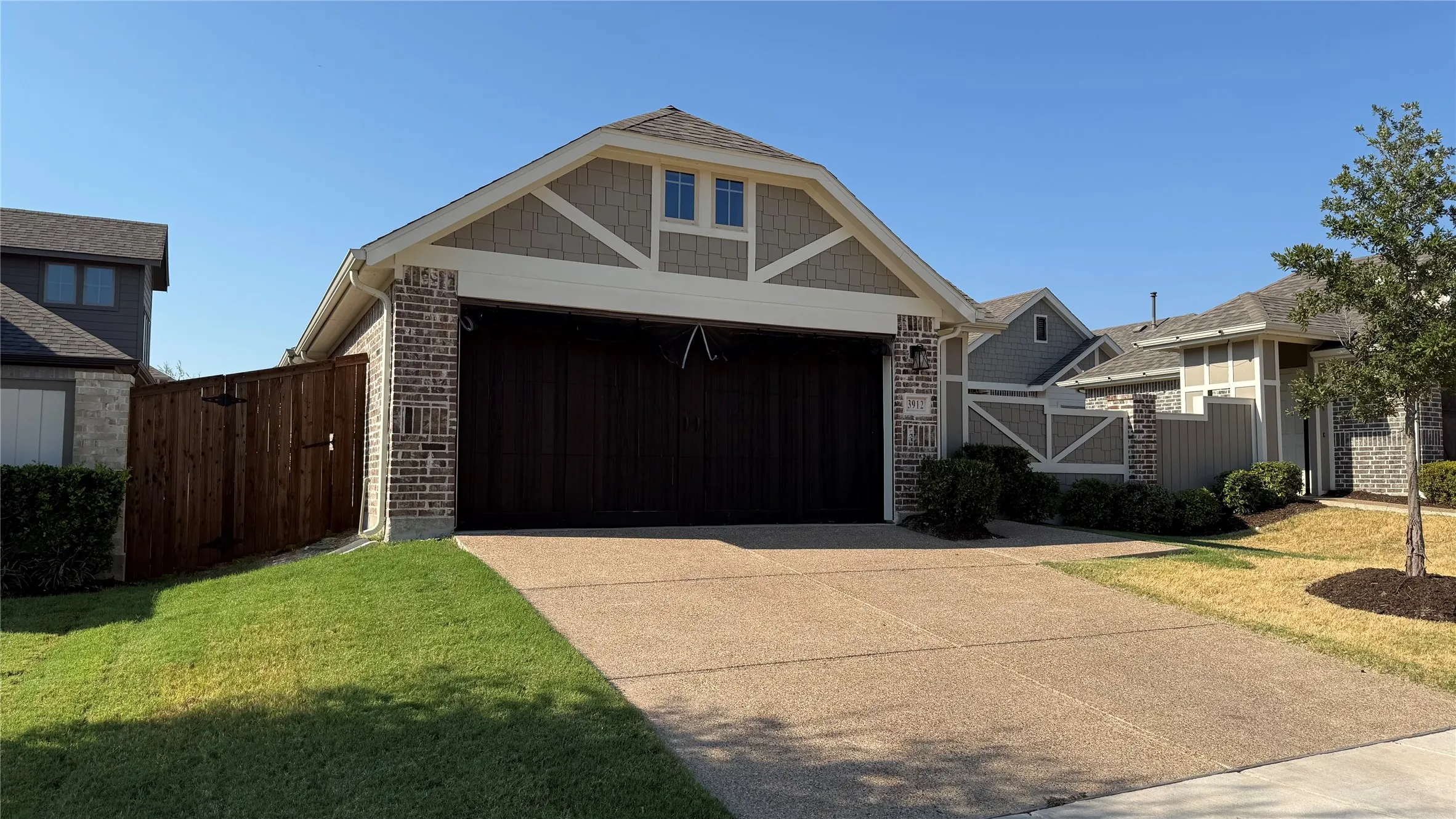 Brick and siding exterior with a peaked roofline, a large dark-toned garage door, and a textured concrete driveway