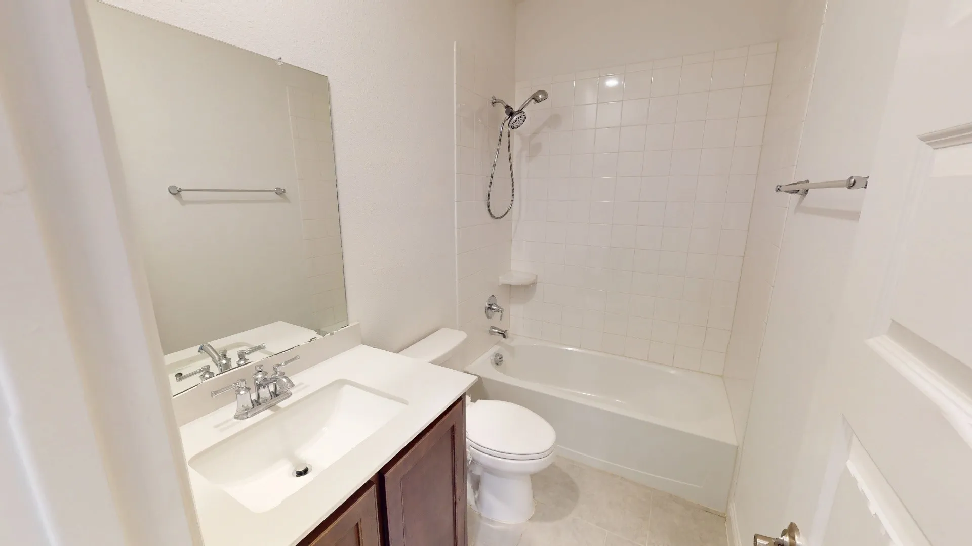 Bathroom with white tile flooring, vanity with integrated sink, chrome faucet, wall-mounted mirror, and a shower/tub combination with white tile surround