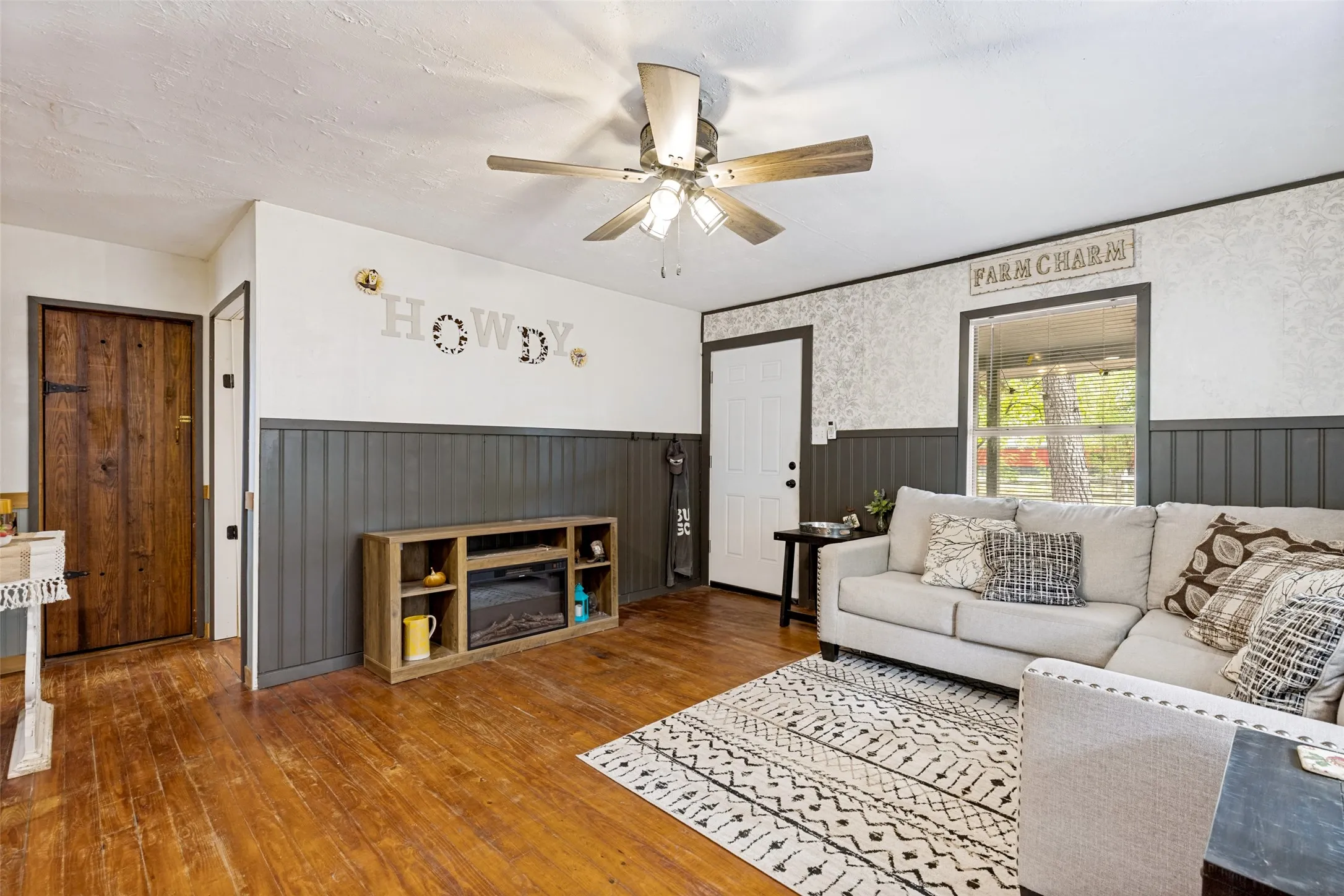Hardwood flooring, painted wainscoting, textured wallpaper, ceiling fan with light fixture, and a window with exterior views