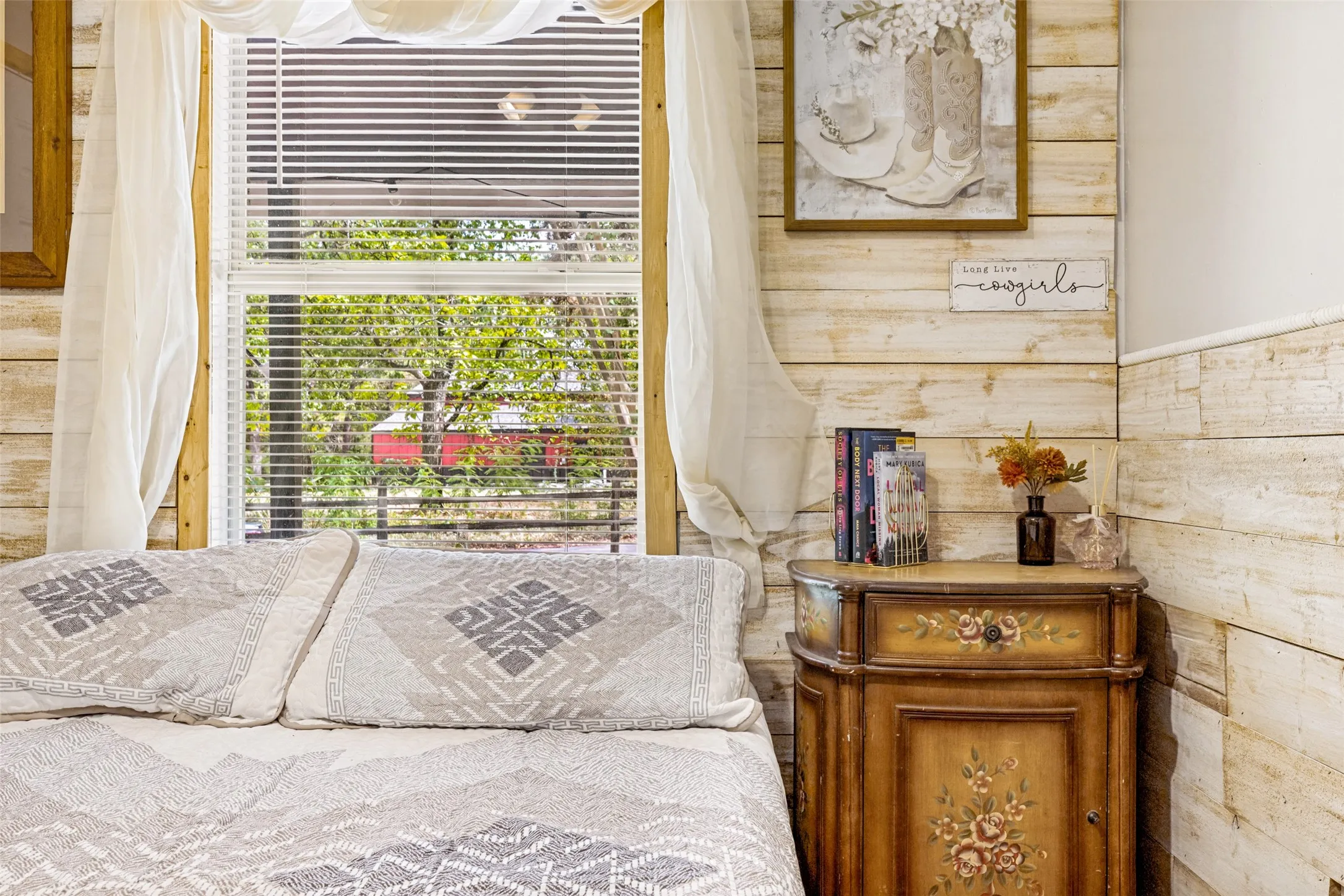 Window with blinds and sheer drapes, wood-finish wall paneling, and a painted wood cabinet