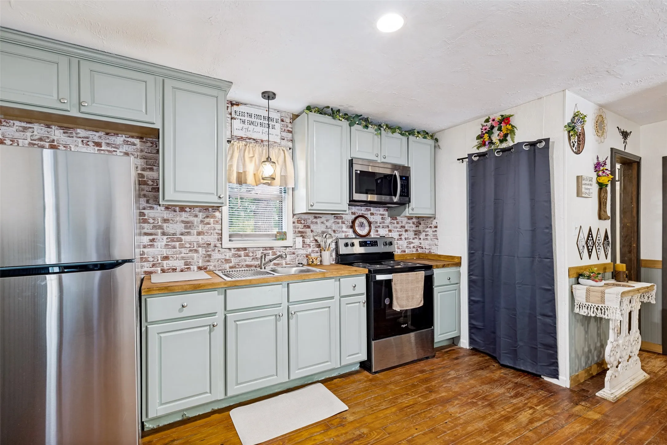 Kitchen featuring light blue cabinetry, wood-finish countertops, stainless steel appliances, and a brick-look backsplash