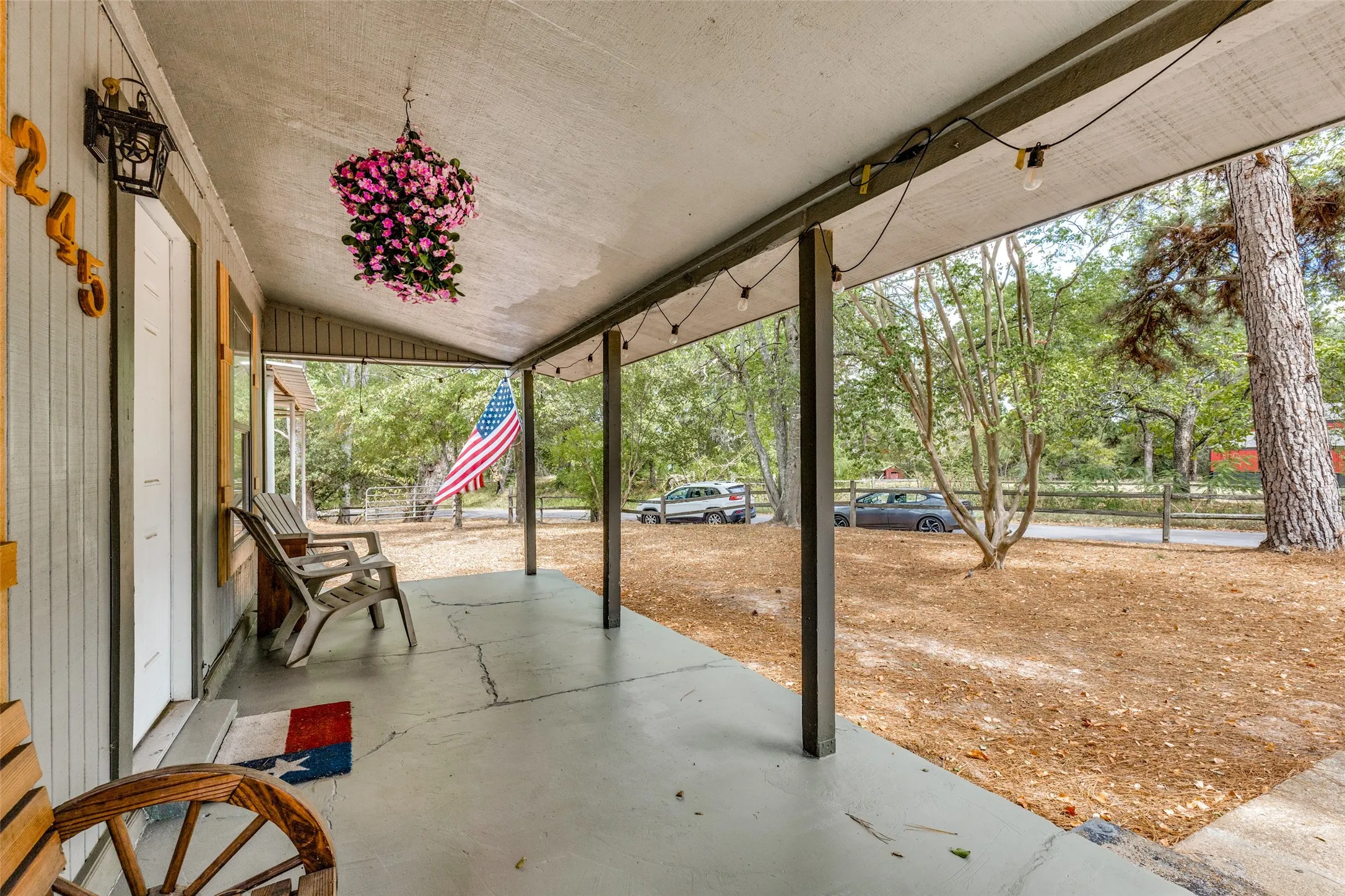 Covered front porch with light gray concrete flooring, dark support columns, and string lighting