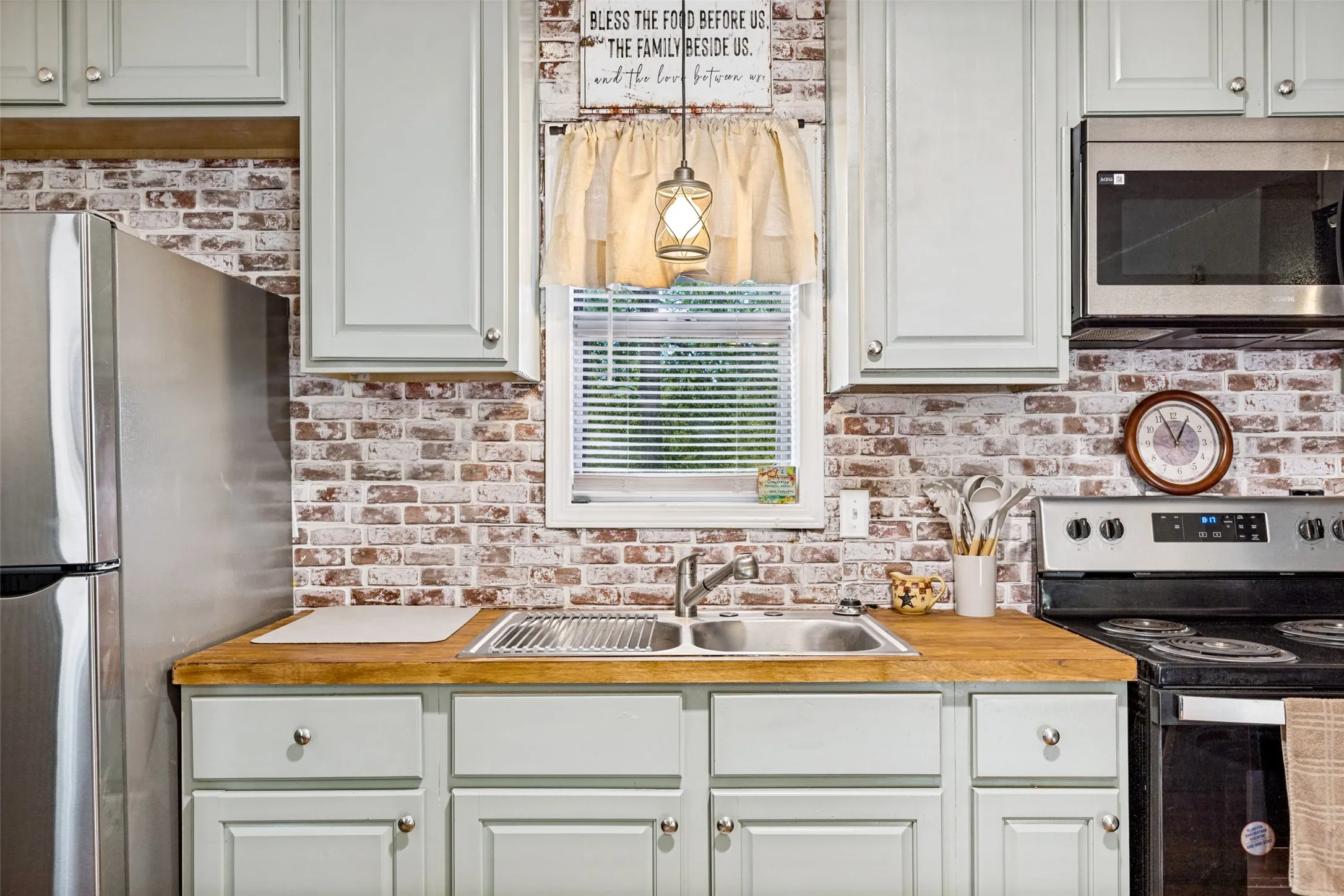 Kitchen featuring light-toned cabinetry, a stainless steel sink, wood-finish countertops, and a brick-finish backsplash