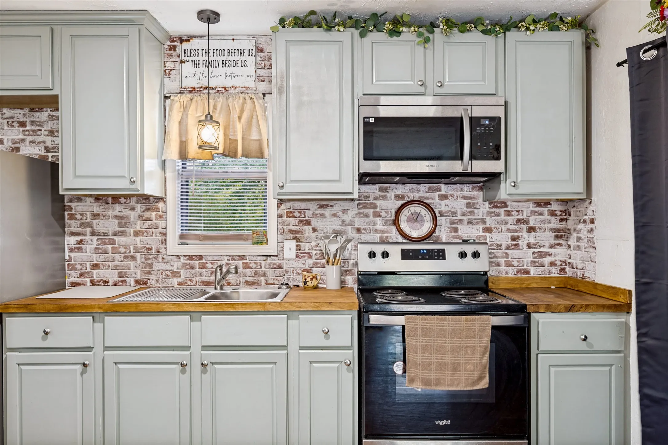 Kitchen featuring light-colored cabinetry, wood-finish countertops, stainless steel appliances, a double basin sink, and a brick-patterned backsplash