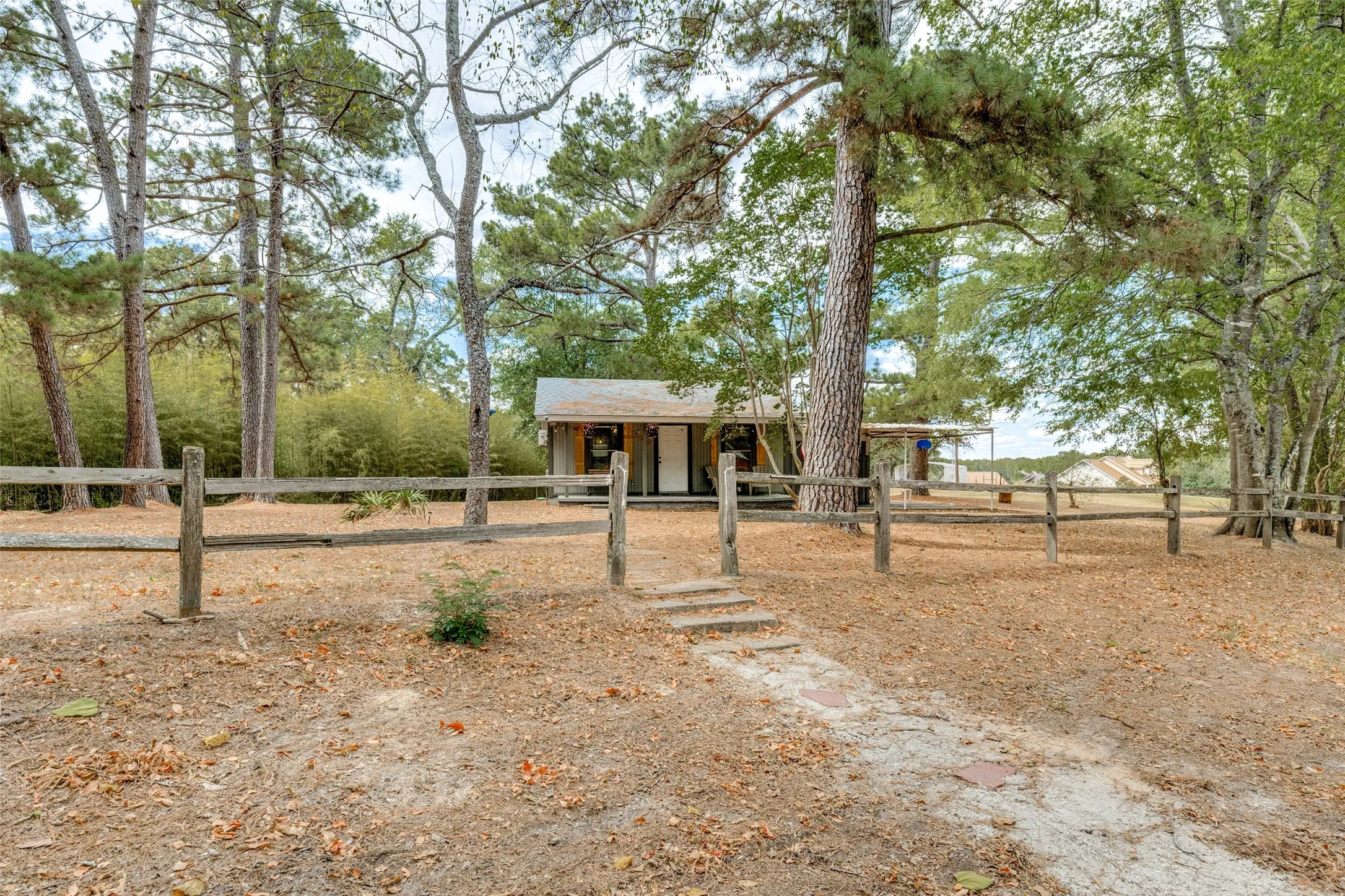 Wood-sided residence surrounded by mature trees, featuring a split-rail fence, stone step pathway, and a covered front entry