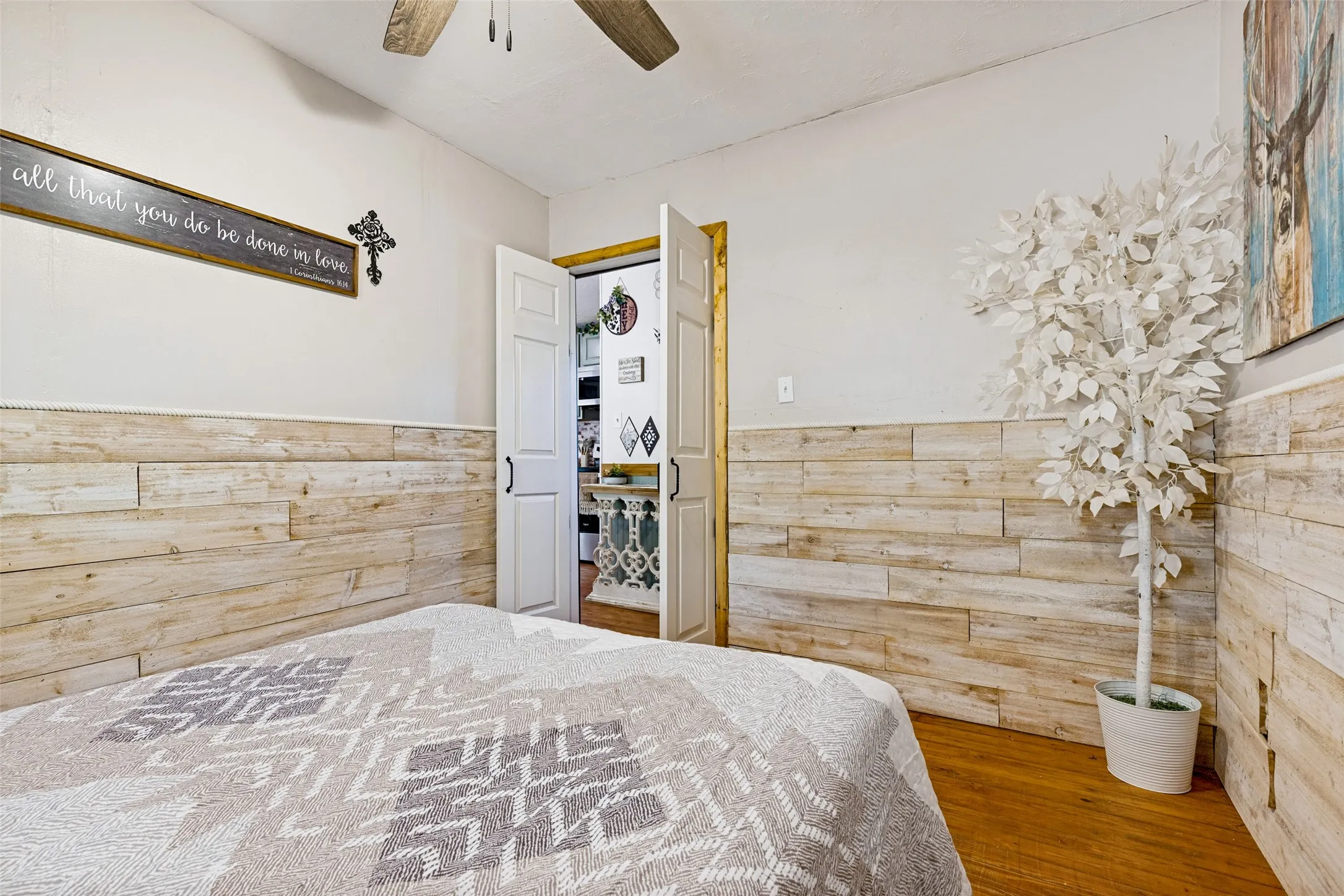Wood-finish flooring, half-wall wood paneling, white painted walls, and a ceiling fan