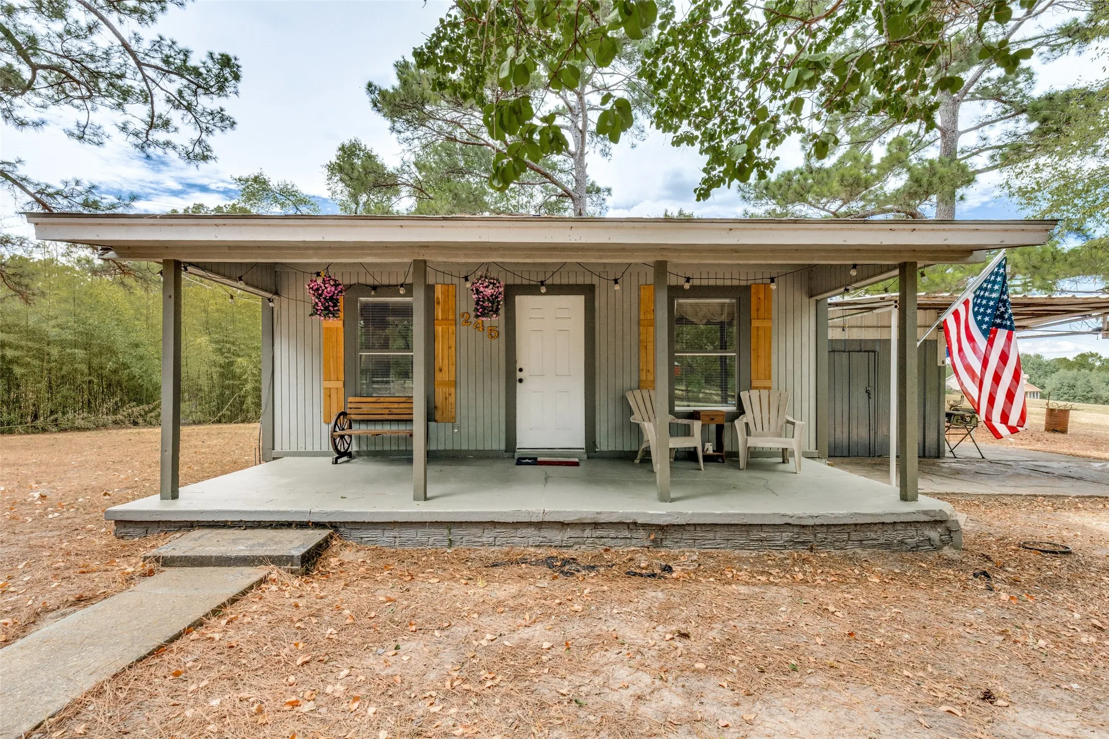 Covered front porch with a concrete slab, textured siding, and wood-toned window shutters