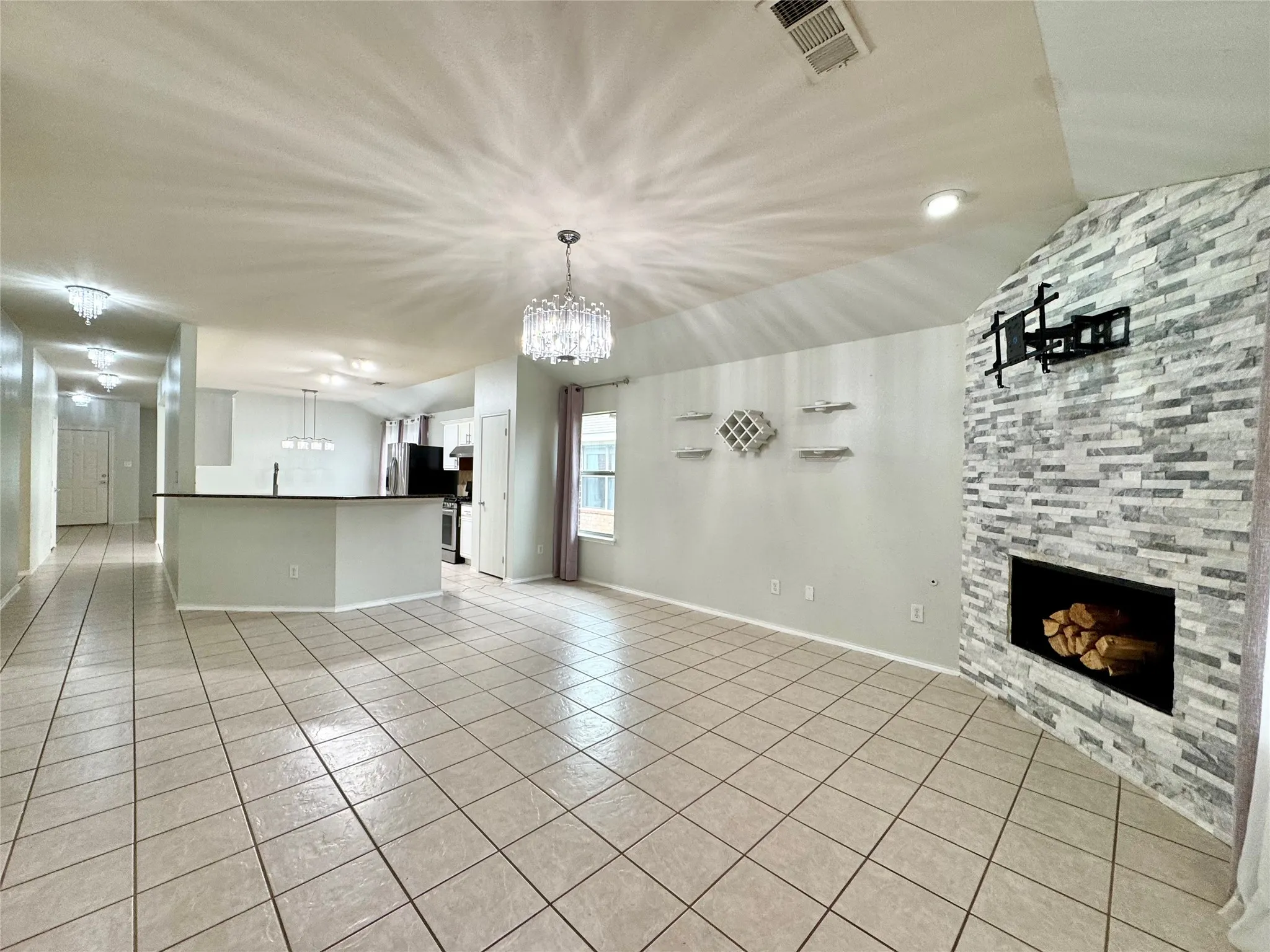 Tile flooring, stone fireplace, crystal chandeliers, built-in shelving, and a kitchen island