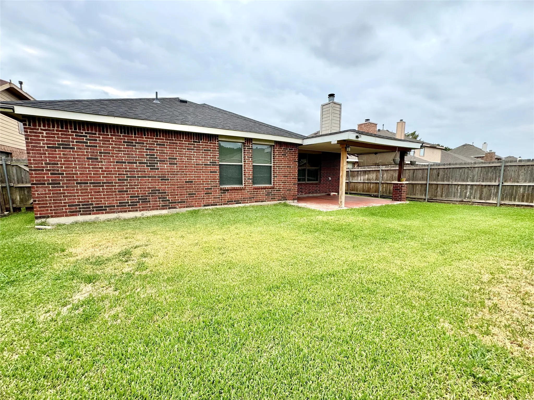 Expansive backyard with a covered patio featuring brick columns and a wood-paneled ceiling