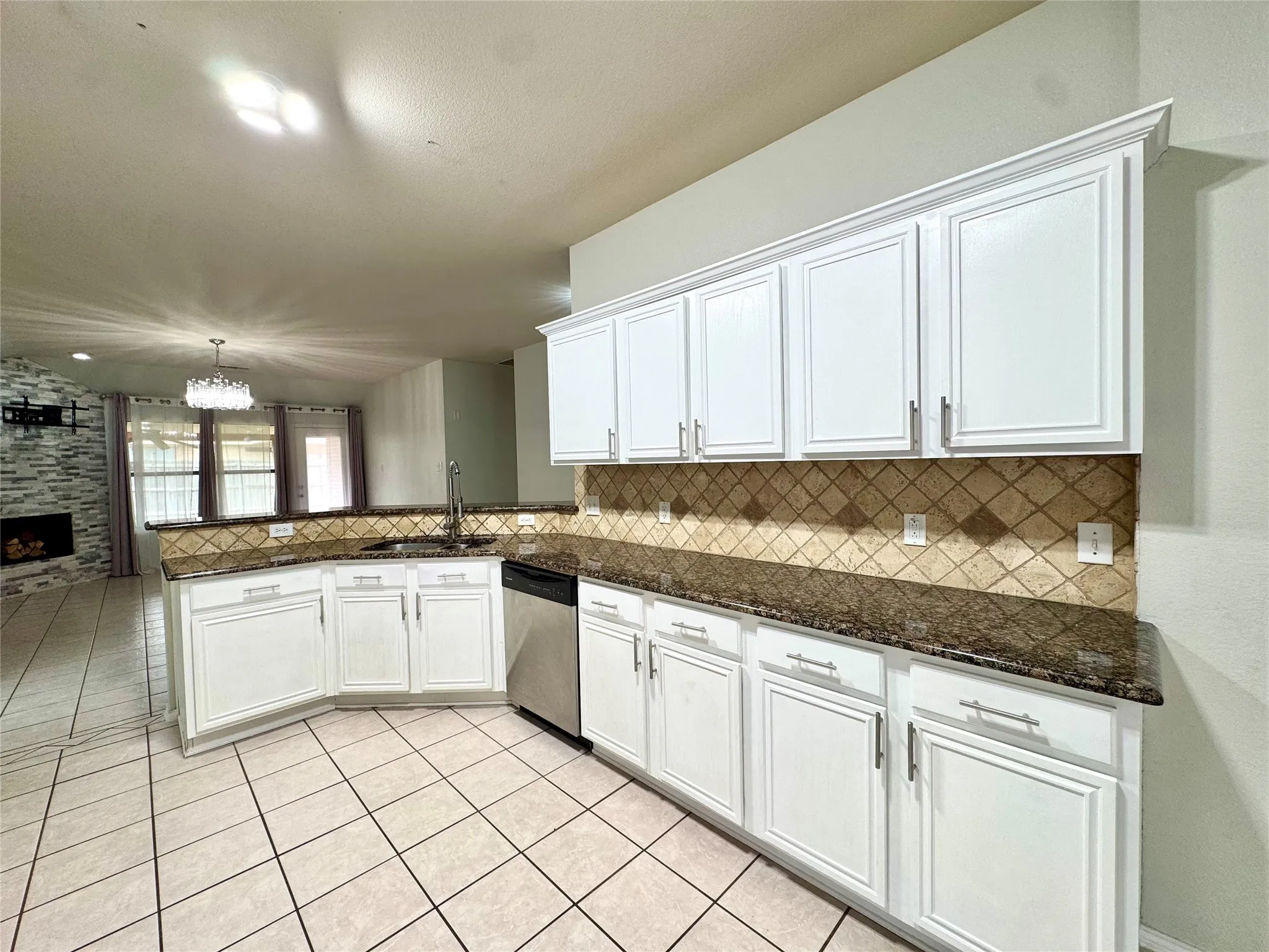 White cabinetry with crown molding, dark stone countertops, stainless steel dishwasher, tile flooring, and a patterned tile backsplash