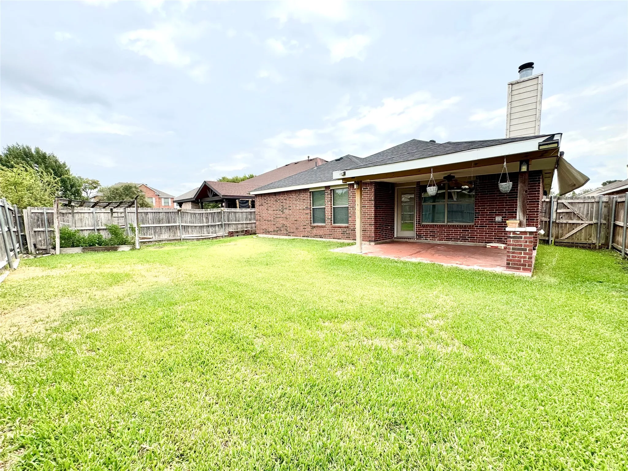 Expansive grassy lawn with a covered patio featuring brick columns, a wood ceiling, and an attached awning