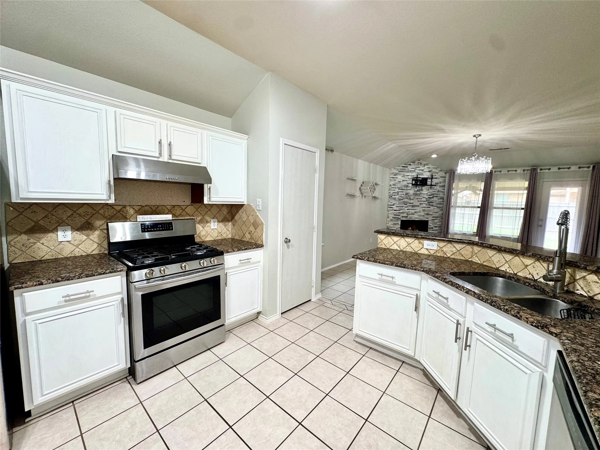 Kitchen featuring white cabinetry, stainless steel range, tiled flooring, granite countertops, and a stone accent wall